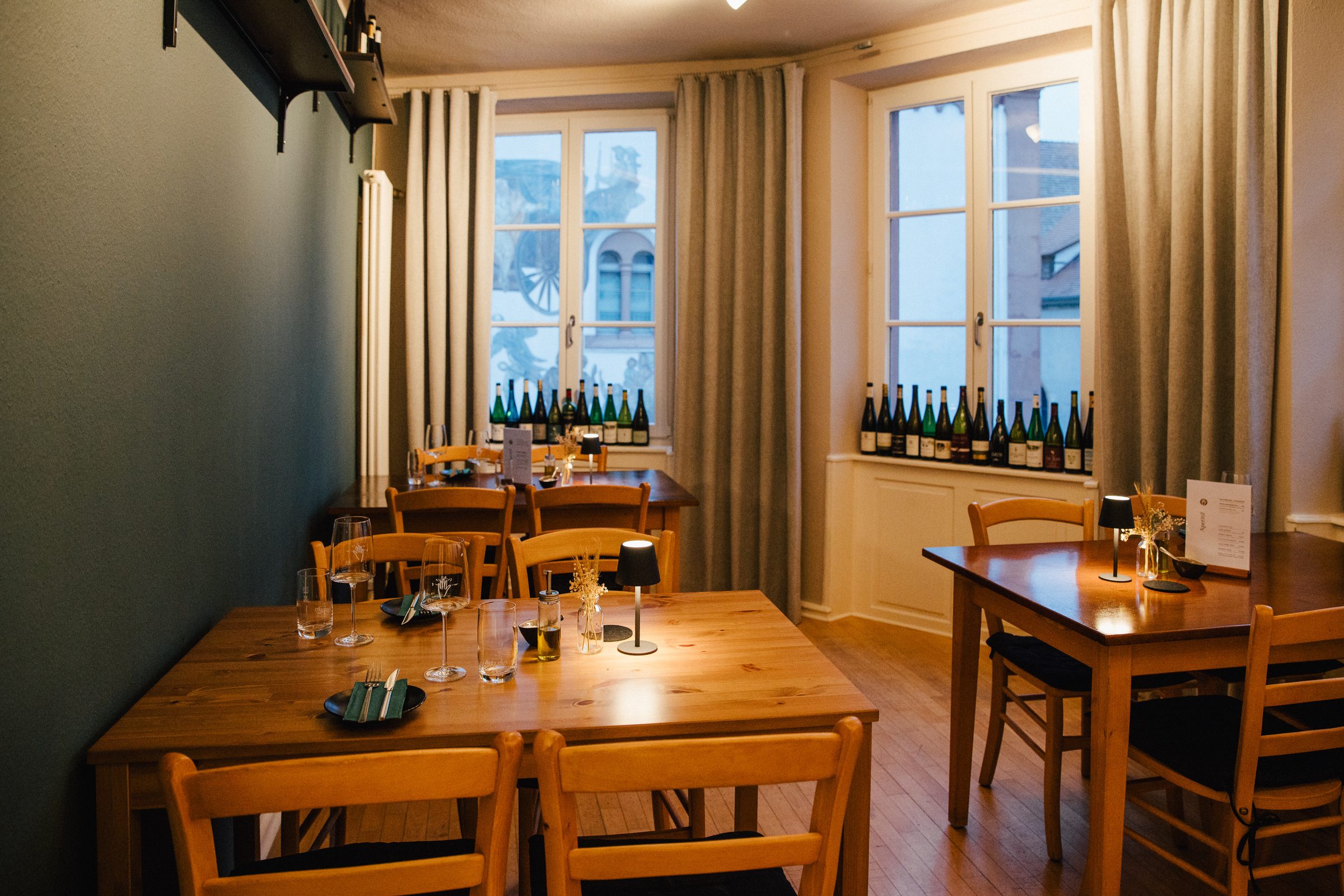 Gastraum im Restaurant 5 Bäuerlein mit gedeckten Holztischen, hohen Sprossenfenstern und Weinflaschen auf den Fensterbänken