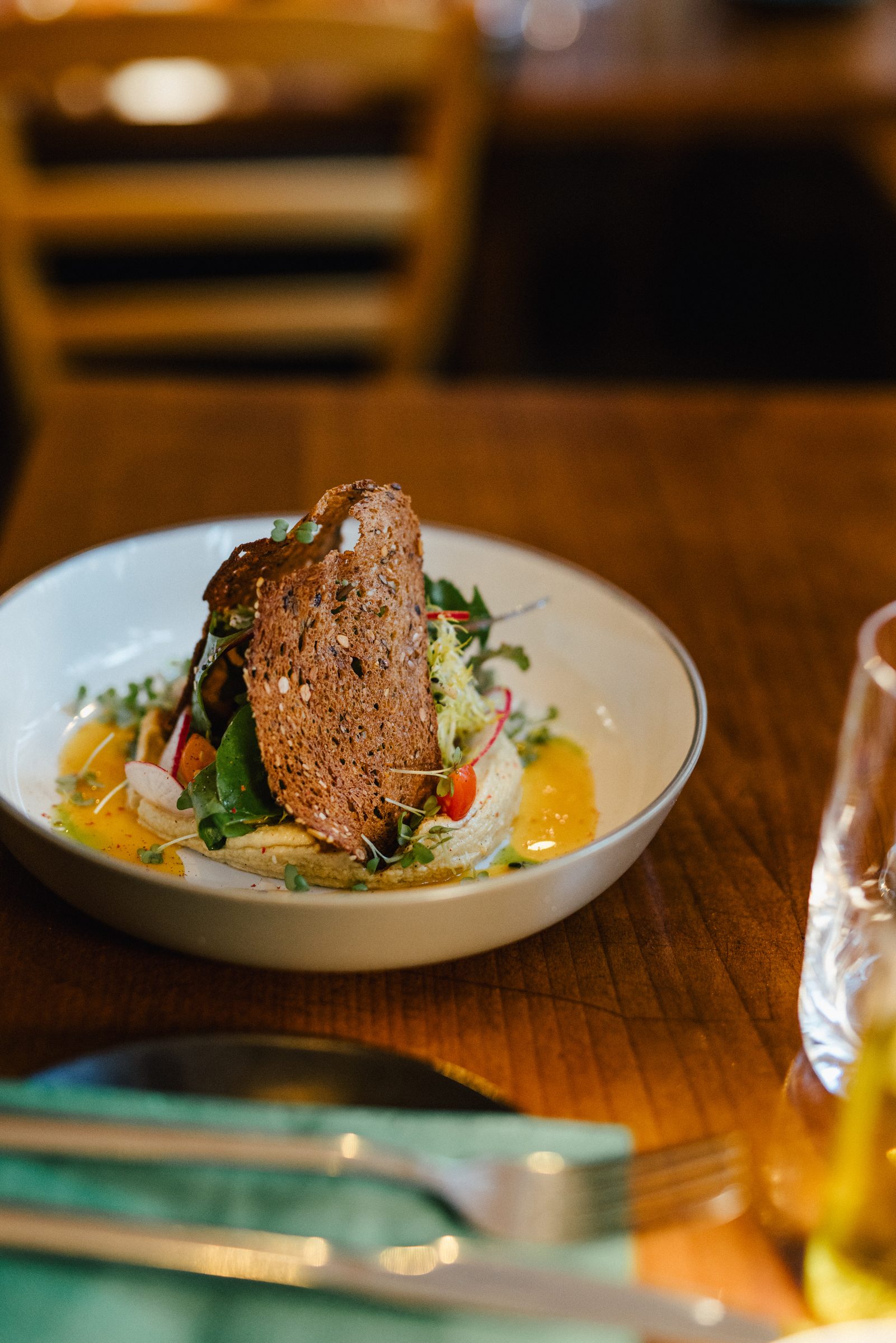 Salat mit knusprigem Vollkornbrot und orangefarbener Sauce in einer weißen Schale, vorne Besteck auf einer petrolfarbenen Serviette
