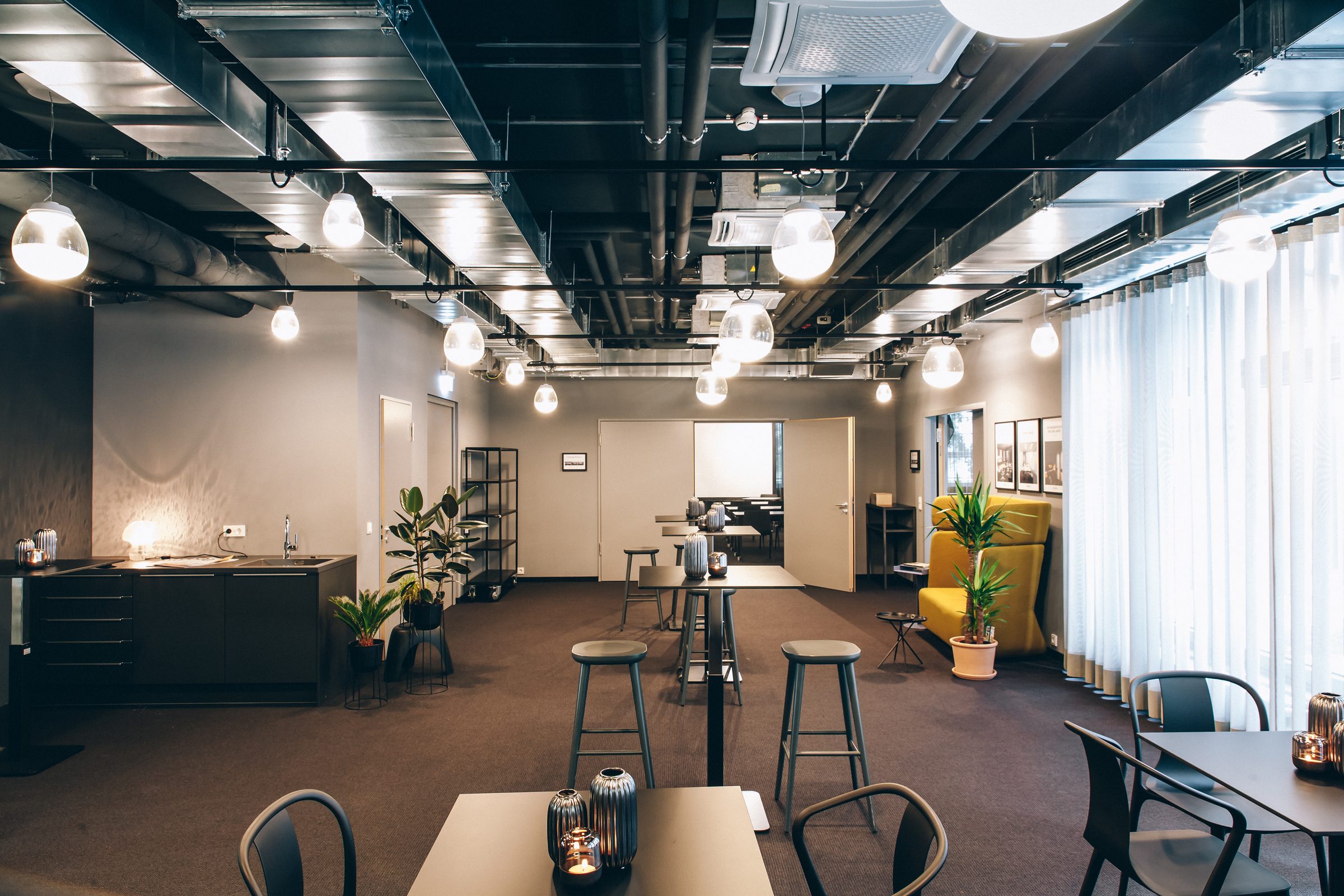 Lounge der Design Offices Stuttgart mit Glas-Pendelleuchten von Artemide über Stehtischen, dahinter Küchenzeile und gelbes Sofa