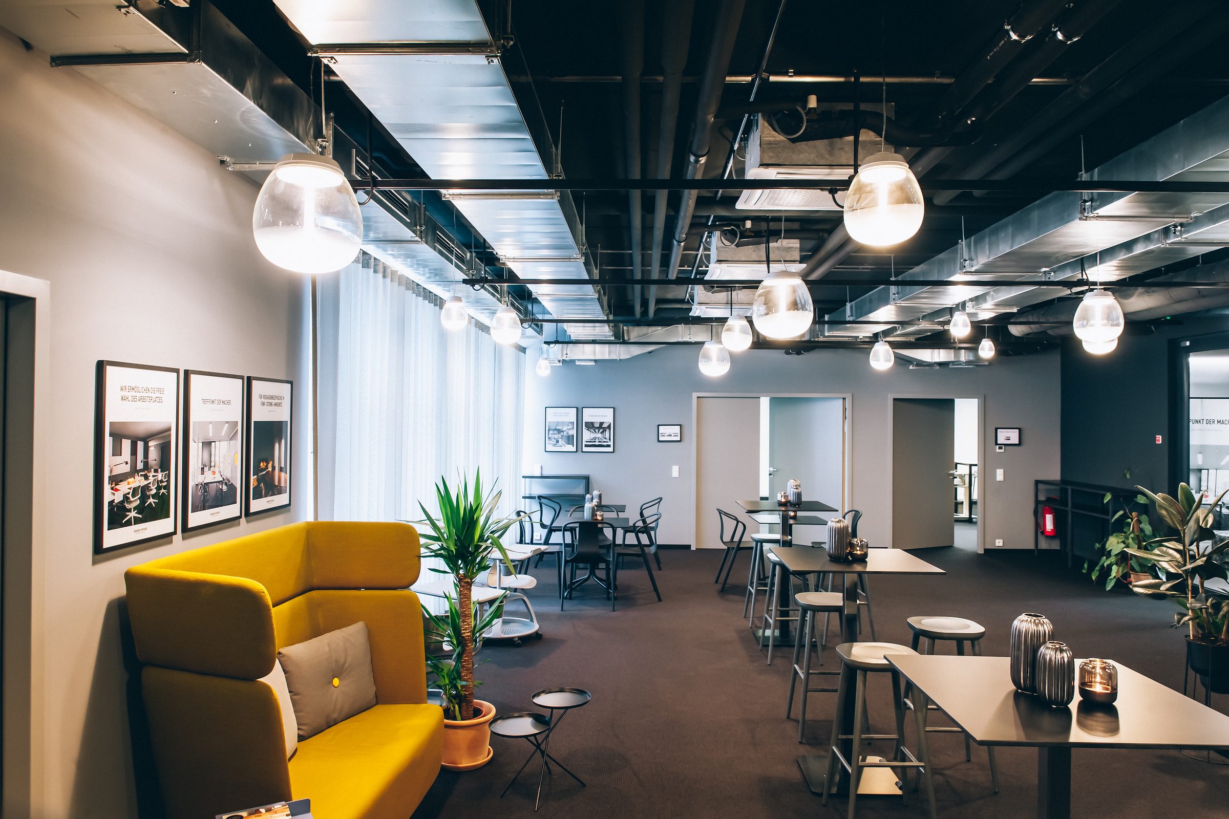 Gelbes Sofa an der Wand und Glas-Pendelleuchten von Artemide über den Stehtischen der Lounge in den Design Offices Stuttgart