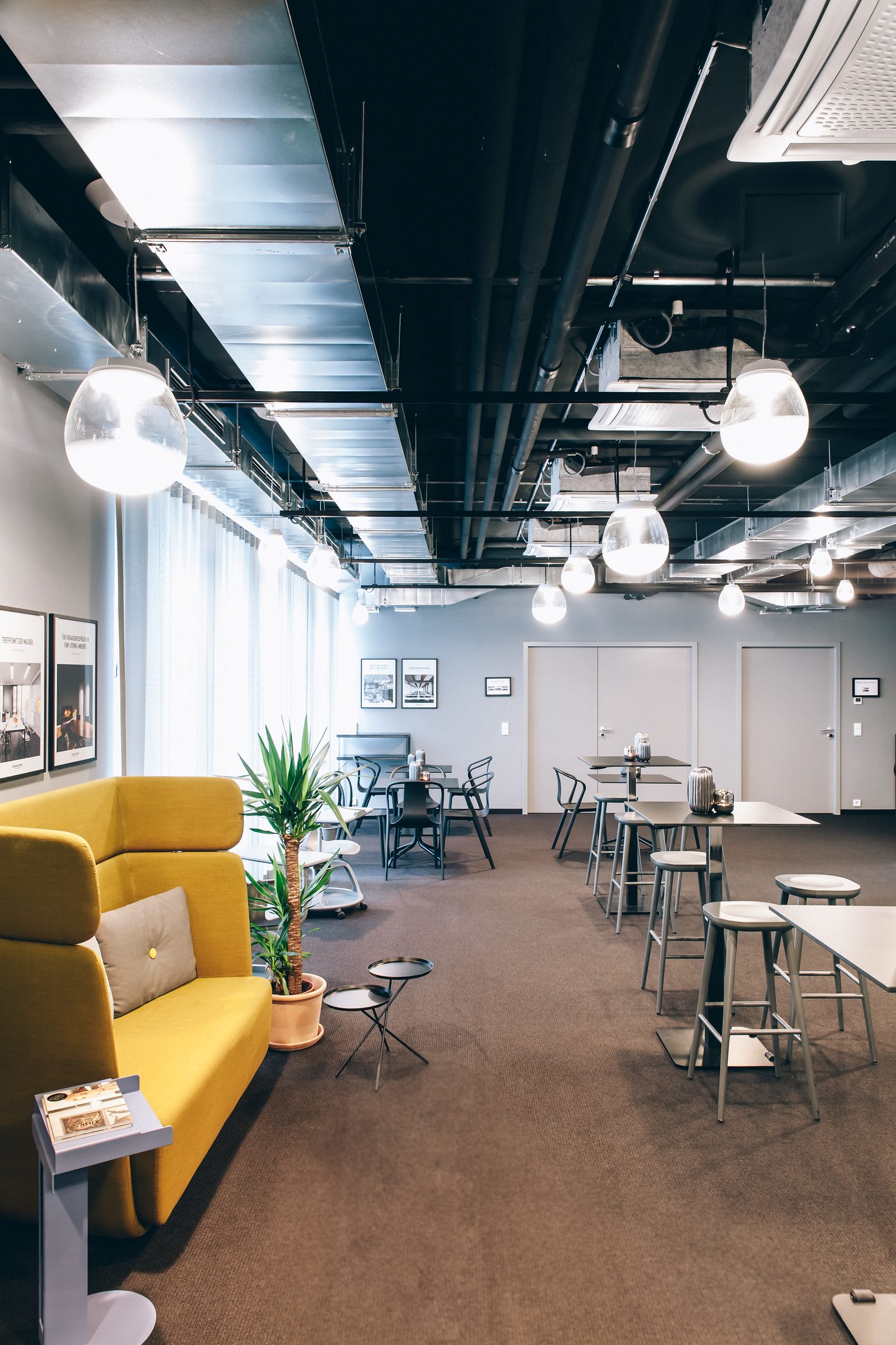 Langgezogene Lounge mit gelbem Sofa, Stehtischen und Pendelleuchten von Artemide in den Design Offices Stuttgart