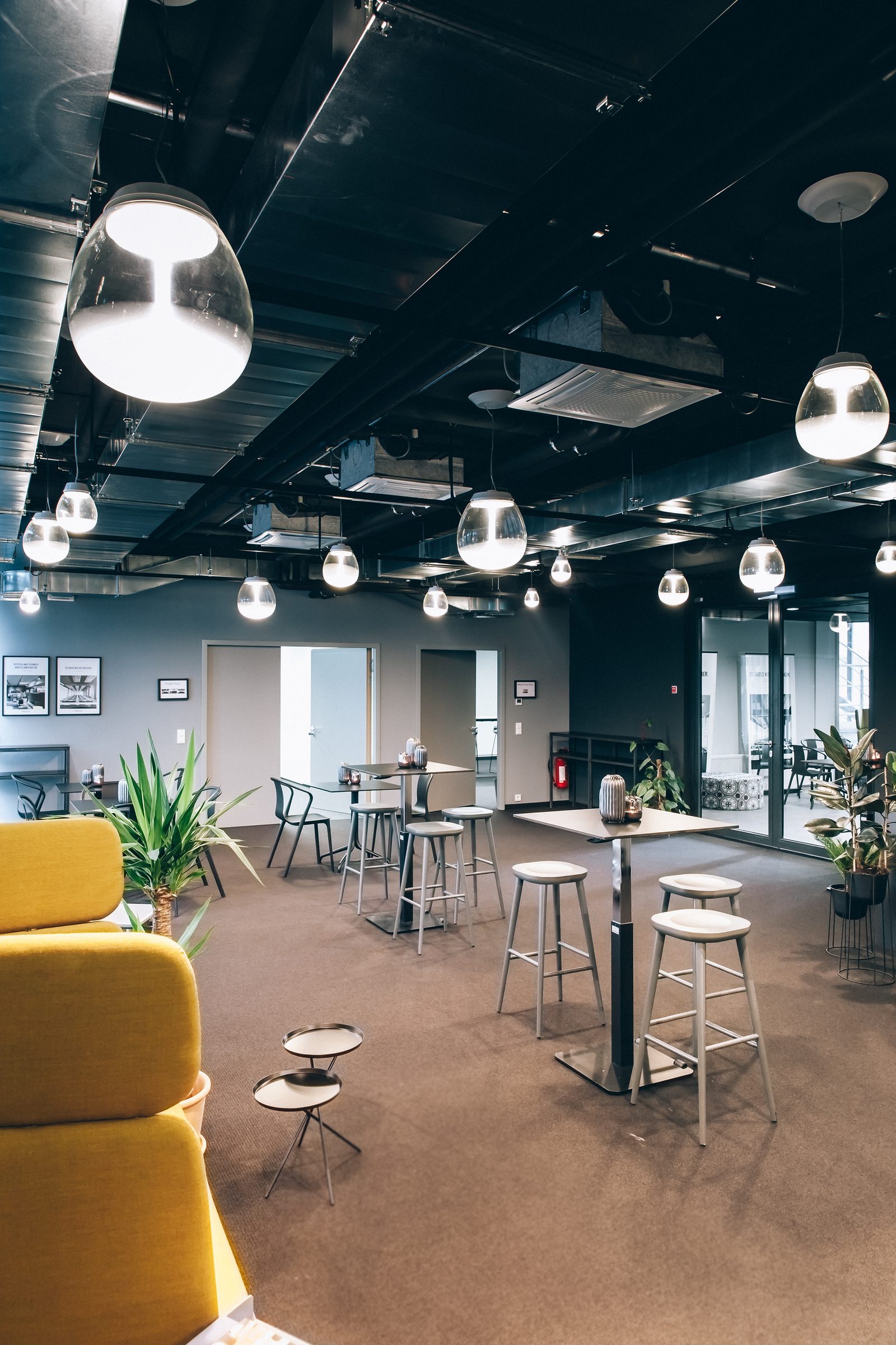 Glas-Pendelleuchten von Artemide über Stehtischen, im Vordergrund ein gelber Sessel, Lounge der Design Offices Stuttgart