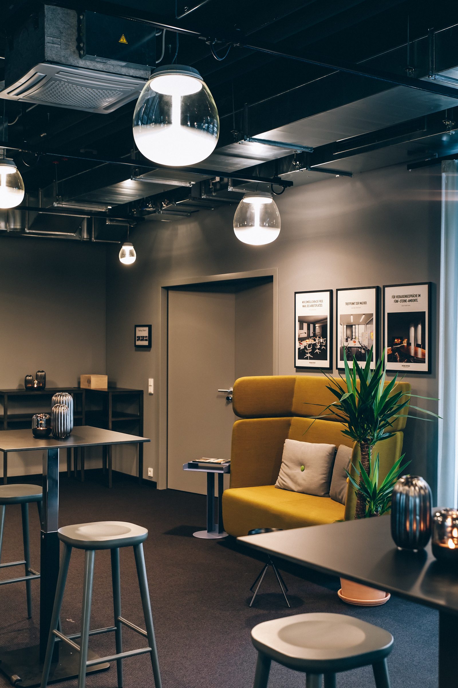 Gelbes Sofa mit Kissen und Pflanze unter Pendelleuchten von Artemide in der Lounge der Design Offices Stuttgart