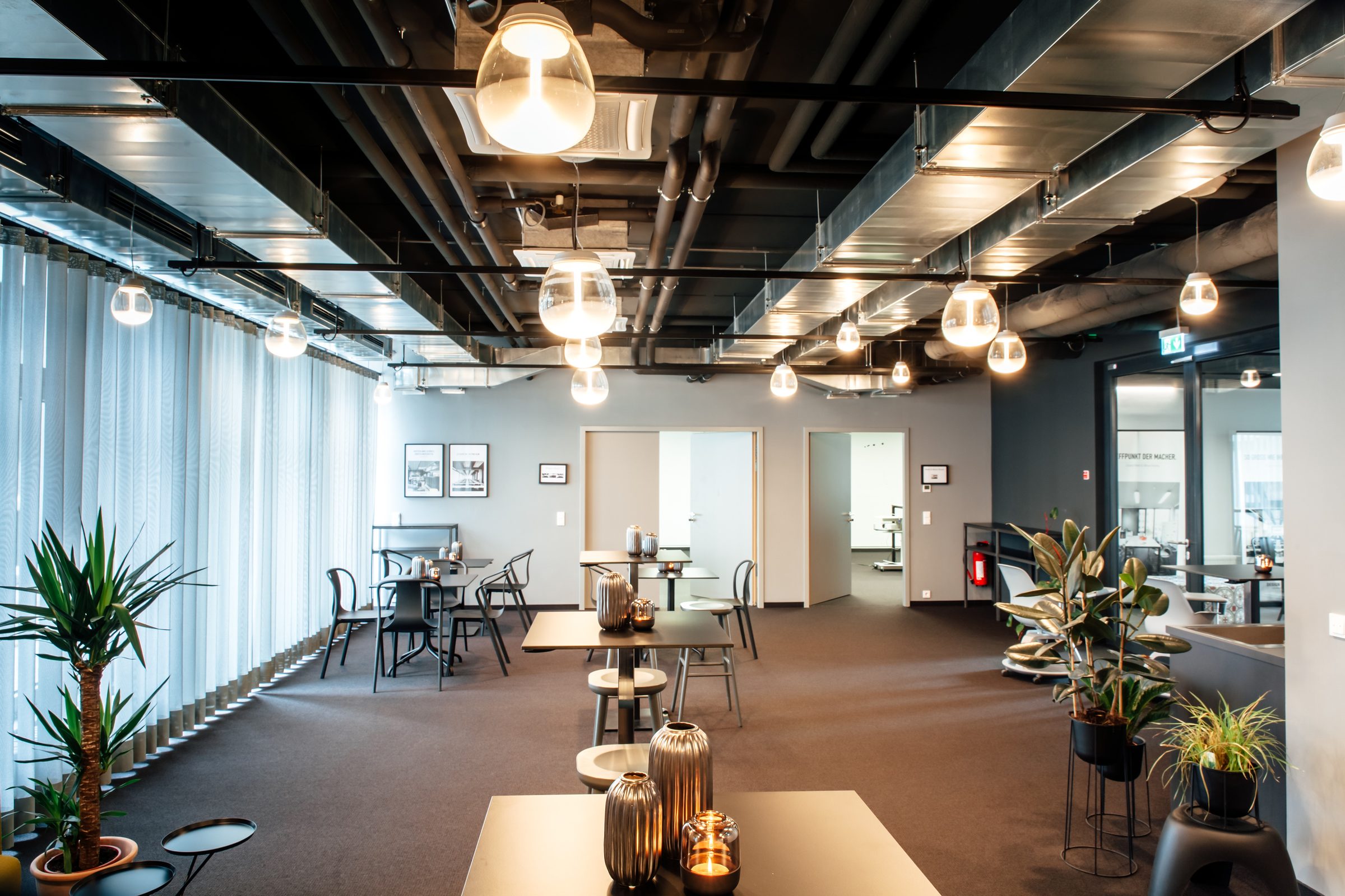 Lounge an der Fensterfront der Design Offices Stuttgart mit Pendelleuchten von Artemide, Tischen, Windlichtern und Pflanzen