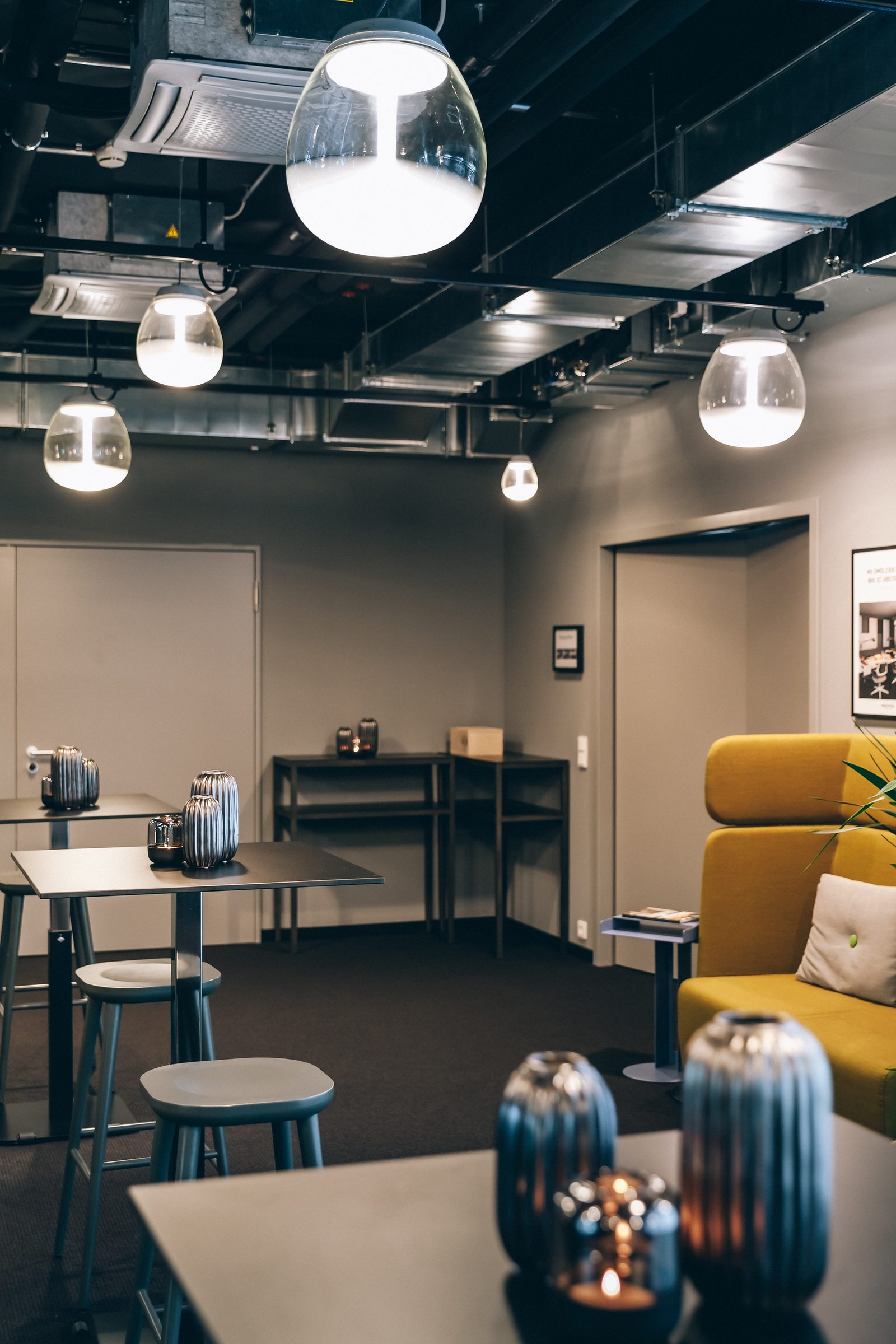 Glas-Pendelleuchte von Artemide über einem Tisch mit Windlichtern, daneben ein gelbes Sofa, Design Offices Stuttgart