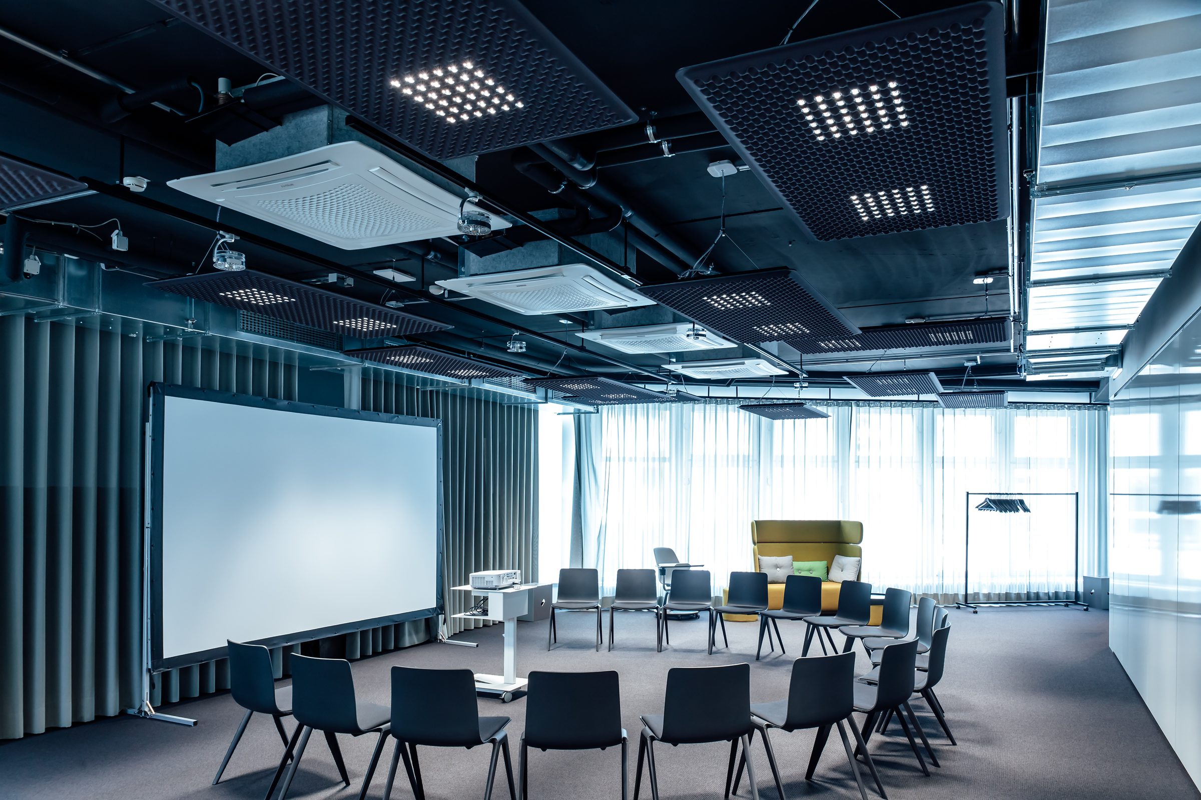 Konferenzraum mit Stuhlkreis, Leinwand und Fensterfront, an der Decke Akustikpaneele mit LED-Leuchten, Design Offices Stuttgart