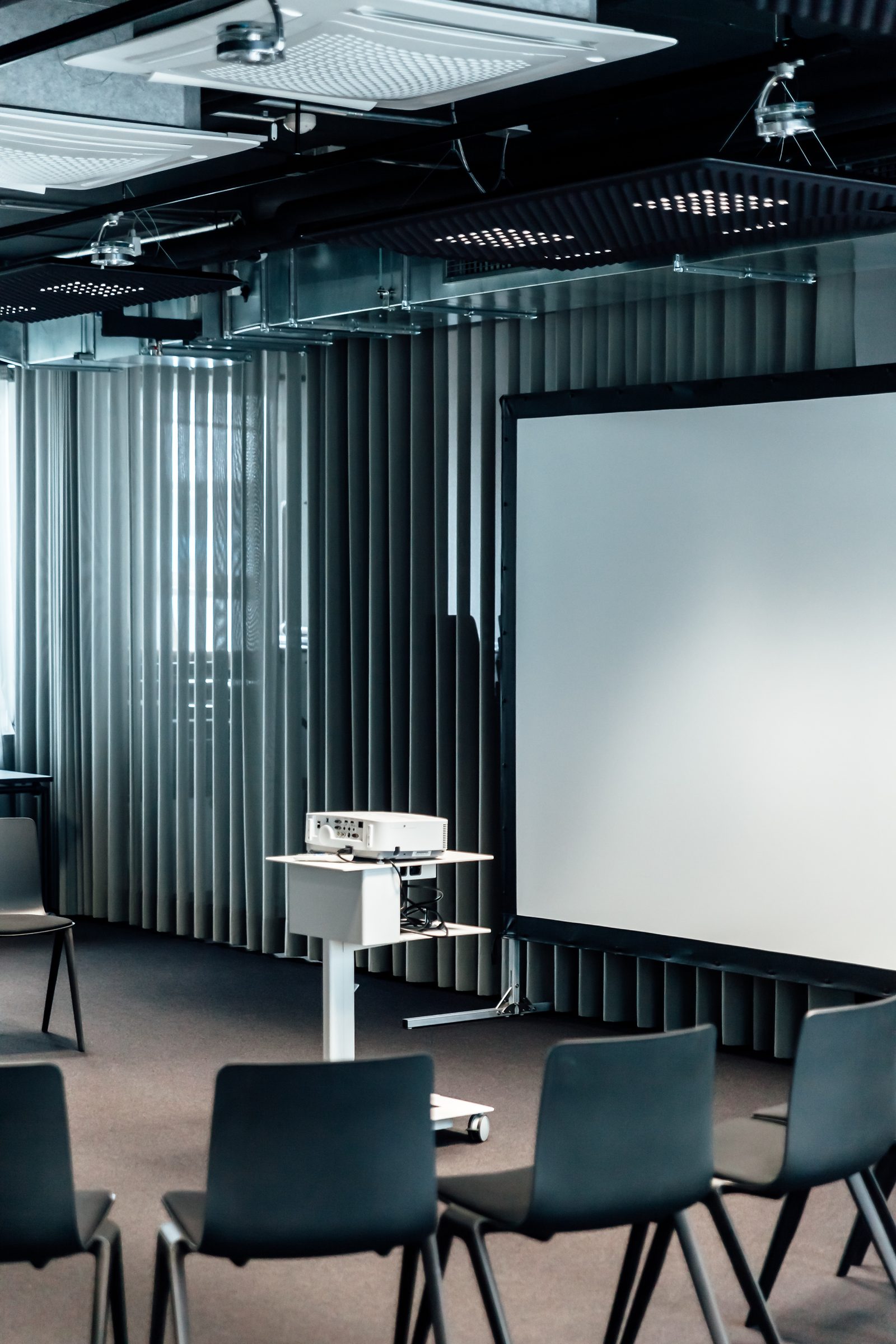 Projektor auf einem Rollwagen vor einer Leinwand und Vorhängen im Konferenzraum der Design Offices Stuttgart