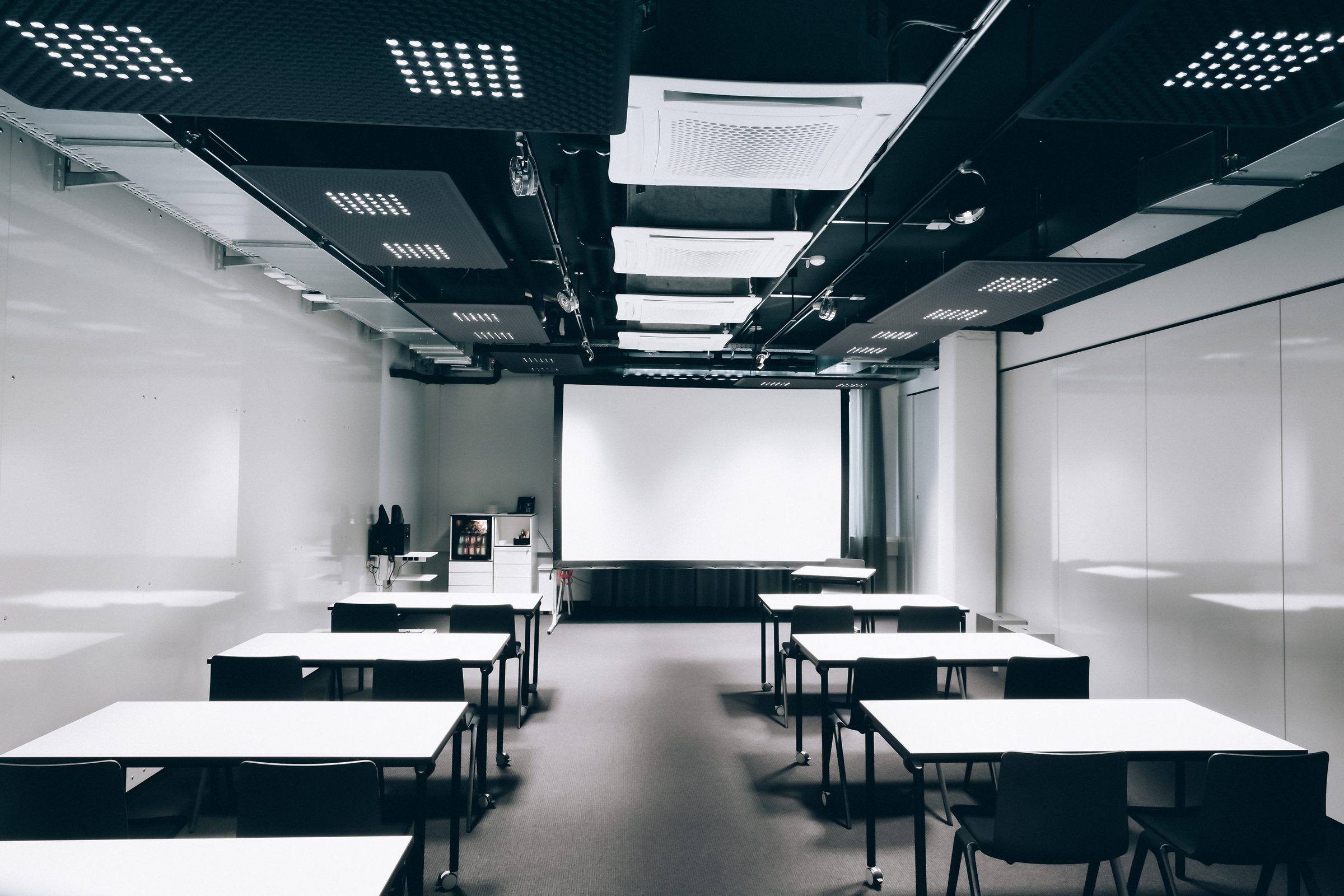 Seminarraum mit weißen Tischreihen und Leinwand, an der Decke Akustikpaneele mit LED-Leuchten, Design Offices Stuttgart