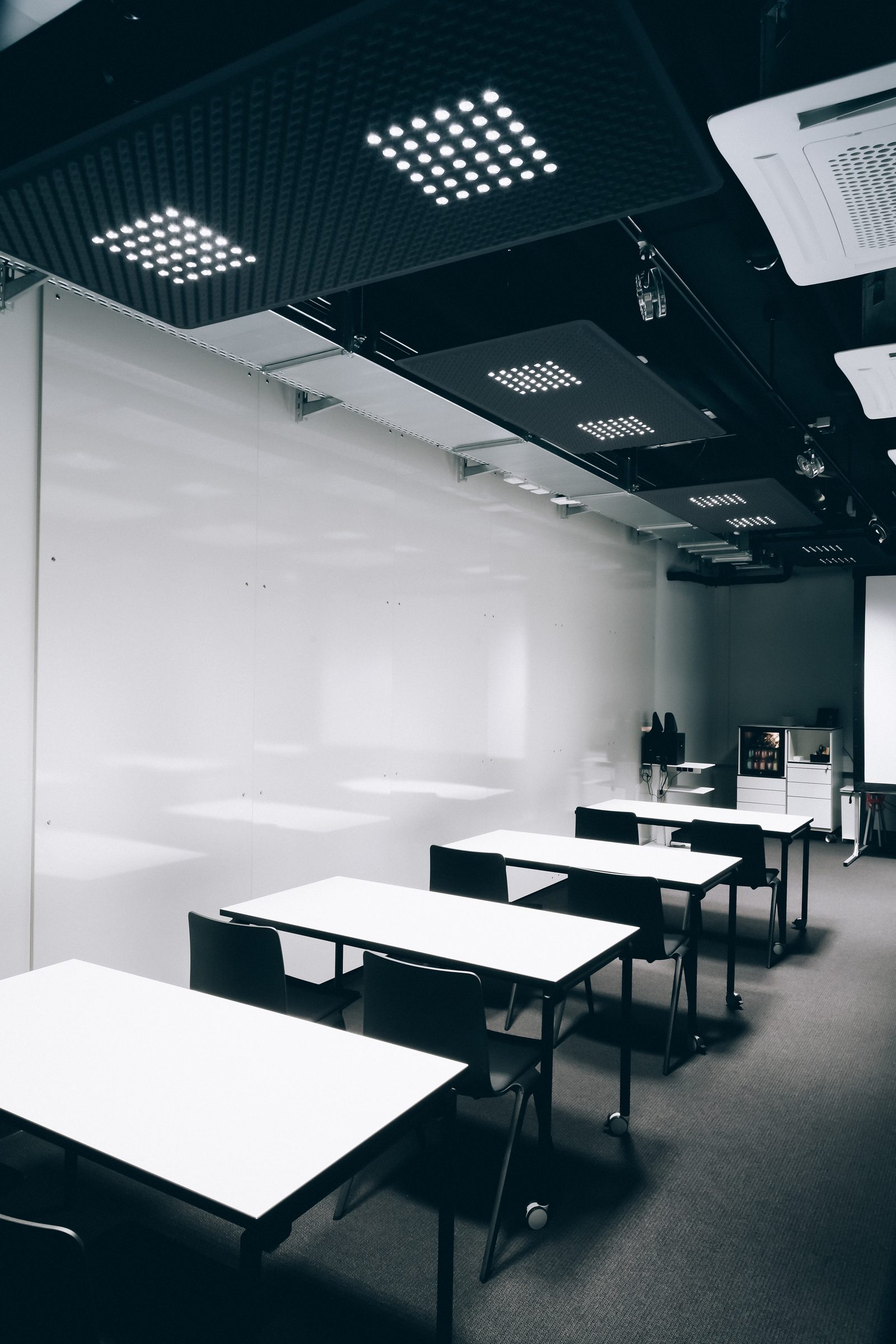 Weiße Tische in einer Reihe unter Akustikpaneelen mit LED-Leuchten im Seminarraum der Design Offices Stuttgart