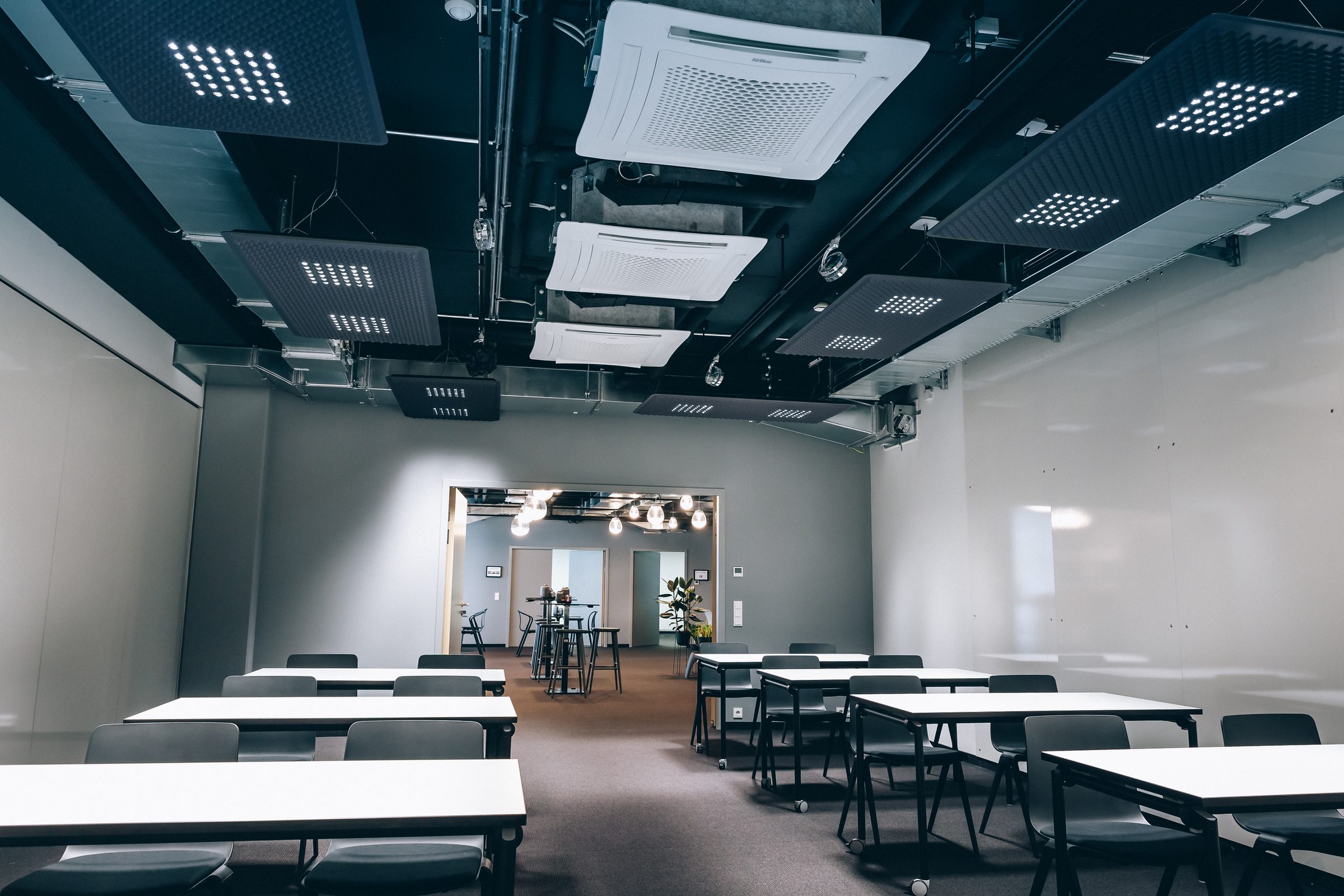 Seminarraum mit Tischreihen, durch die offene Tür Blick in die Lounge mit Pendelleuchten, Design Offices Stuttgart