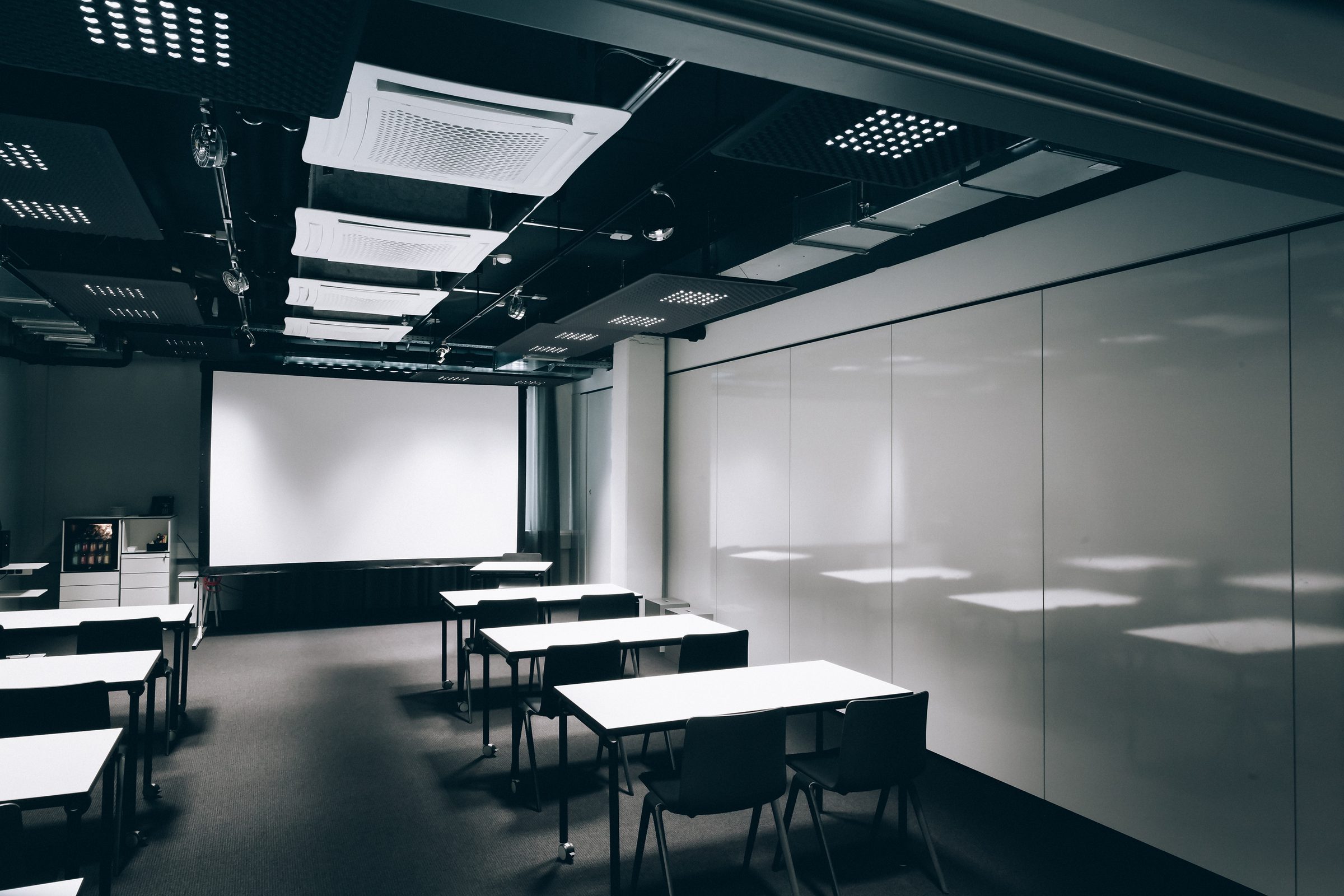 Seminarraum mit Leinwand und Tischreihen entlang einer hellen Wand, Design Offices Stuttgart