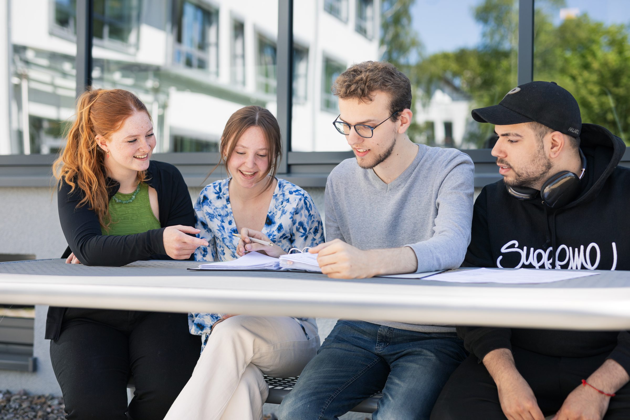 Vier junge Leute arbeiten gemeinsam an einem Tisch auf dem Campus von BIHA Hörakustik