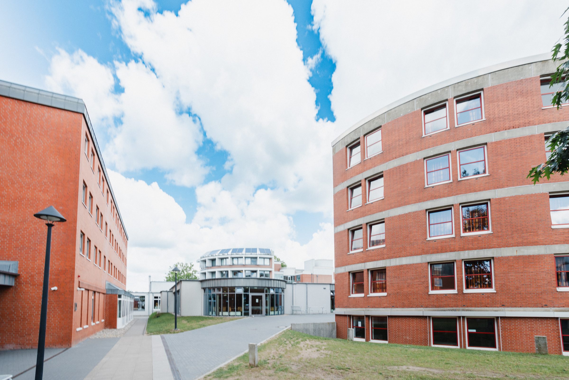 Campus von BIHA Hörakustik mit Backsteingebäuden, dazwischen der Weg zum runden Hauptgebäude