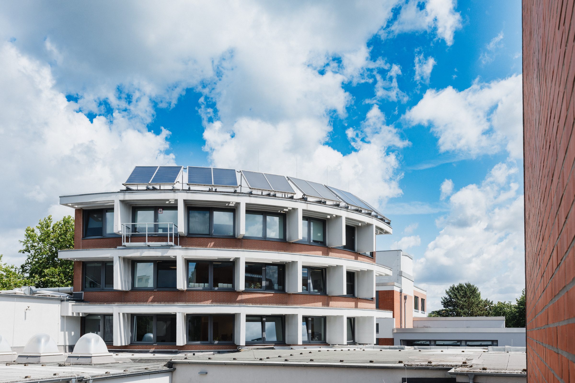 Rundes Gebäude mit Solarmodulen auf dem Dach auf dem Campus von BIHA Hörakustik unter blauem Himmel mit Wolken