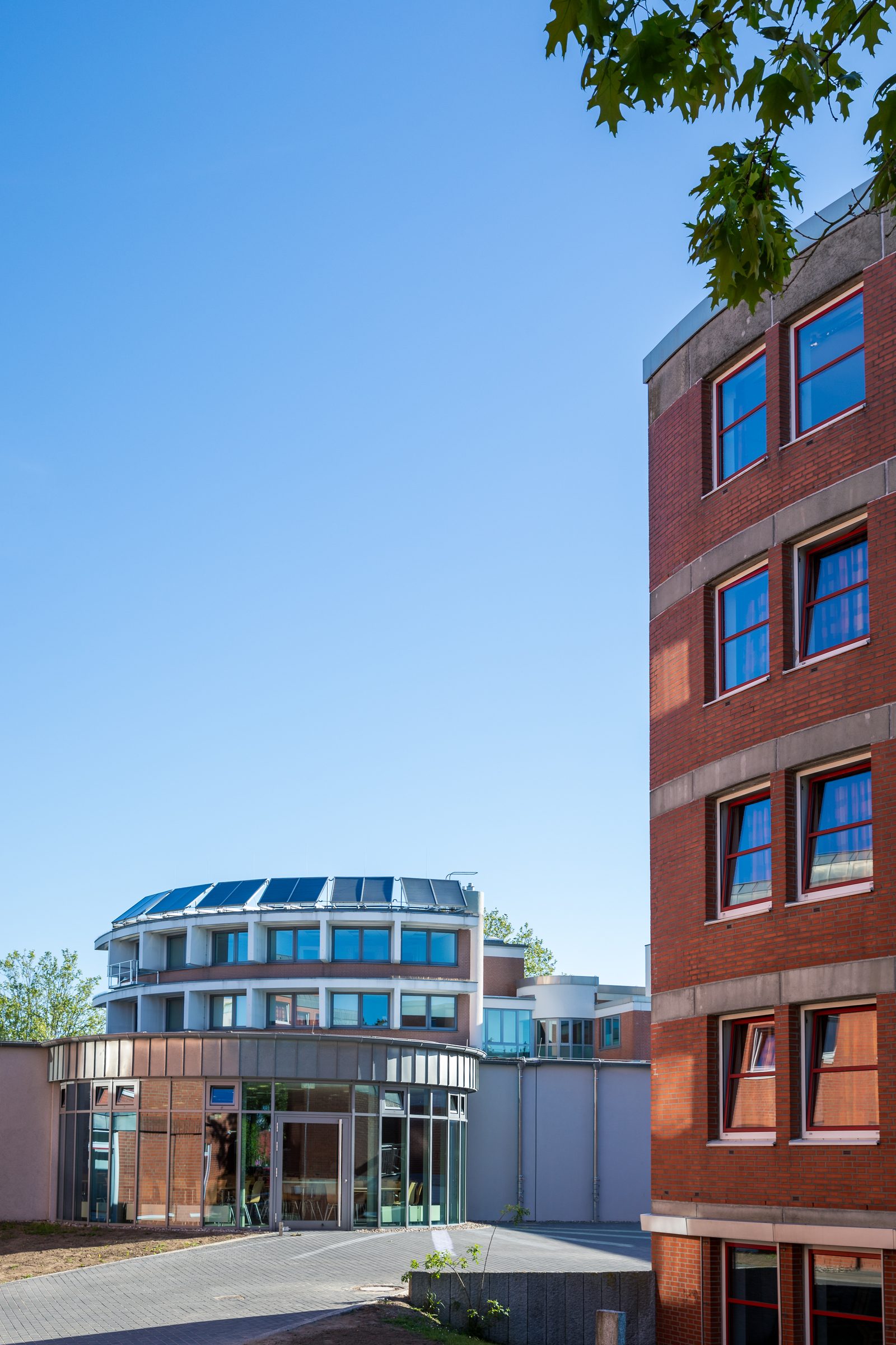 Backsteingebäude und rundes Gebäude mit Glasfront auf dem Campus von BIHA Hörakustik vor blauem Himmel