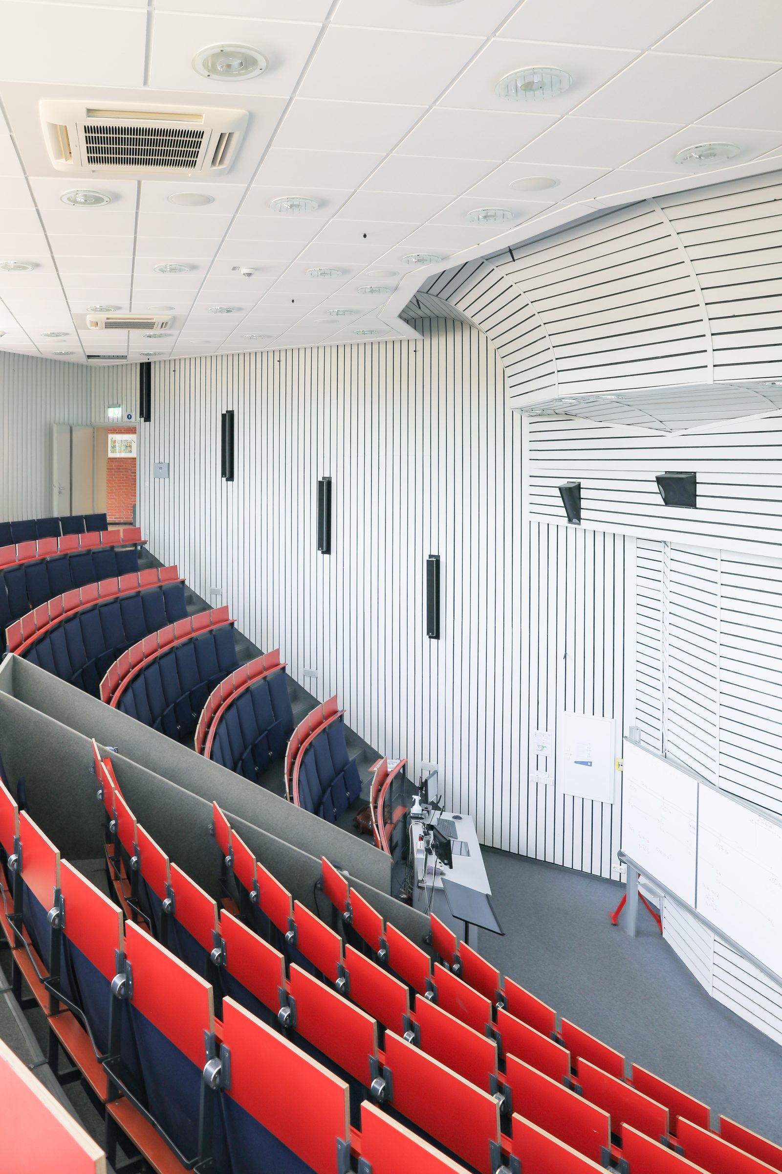 Hörsaal von BIHA Hörakustik mit roten Sitzreihen und weißer Lamellenwand, von oben fotografiert