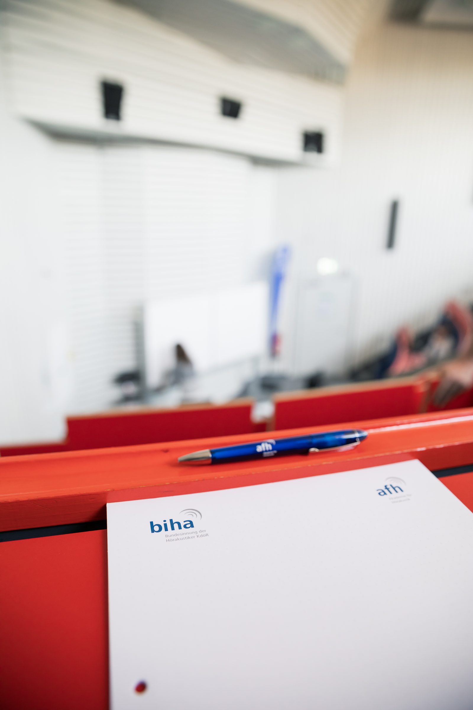 Schreibblock mit biha-Logo und Kugelschreiber auf einem roten Pult im Hörsaal
