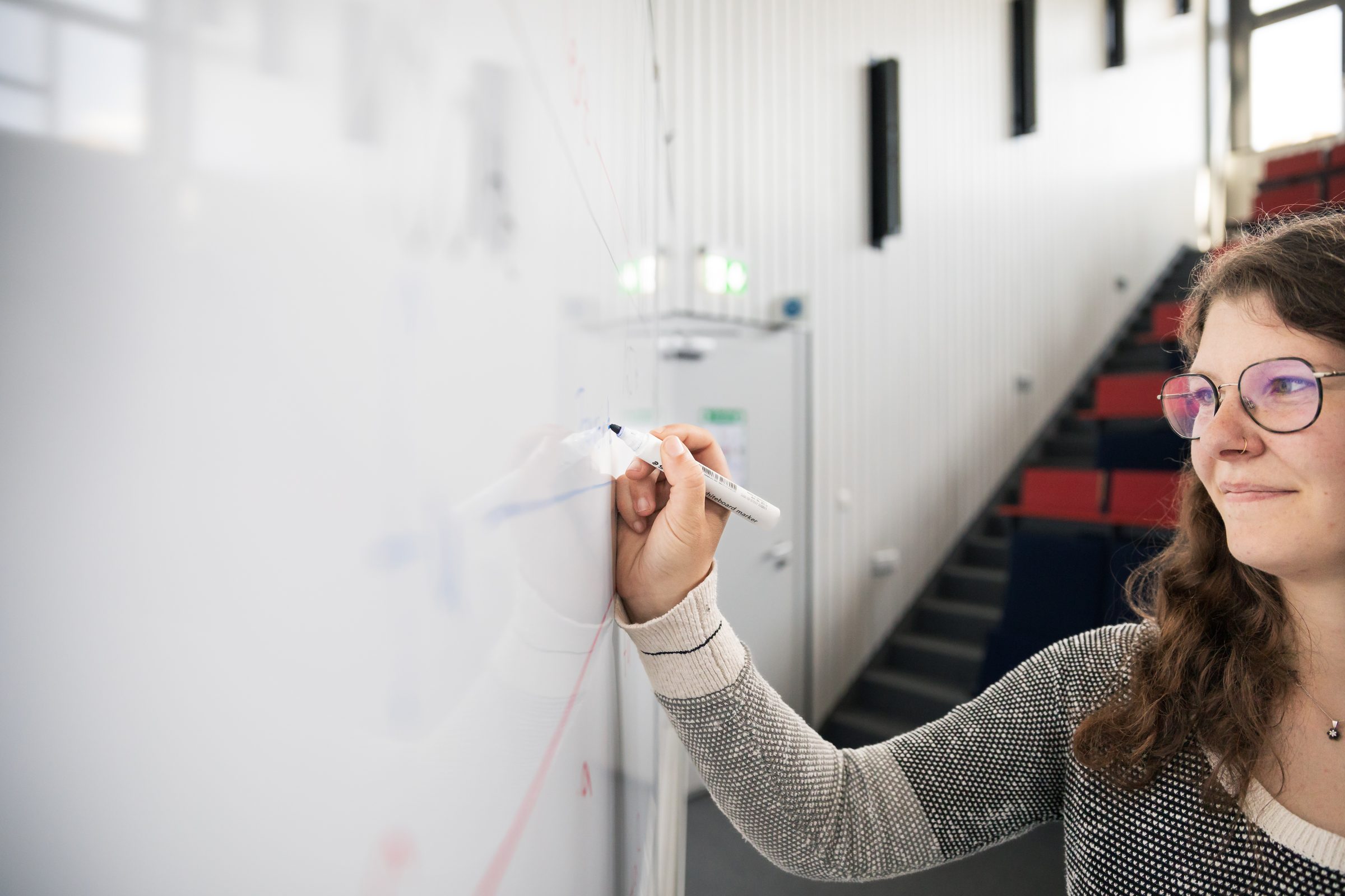 Junge Frau schreibt im Hörsaal von BIHA Hörakustik an ein Whiteboard