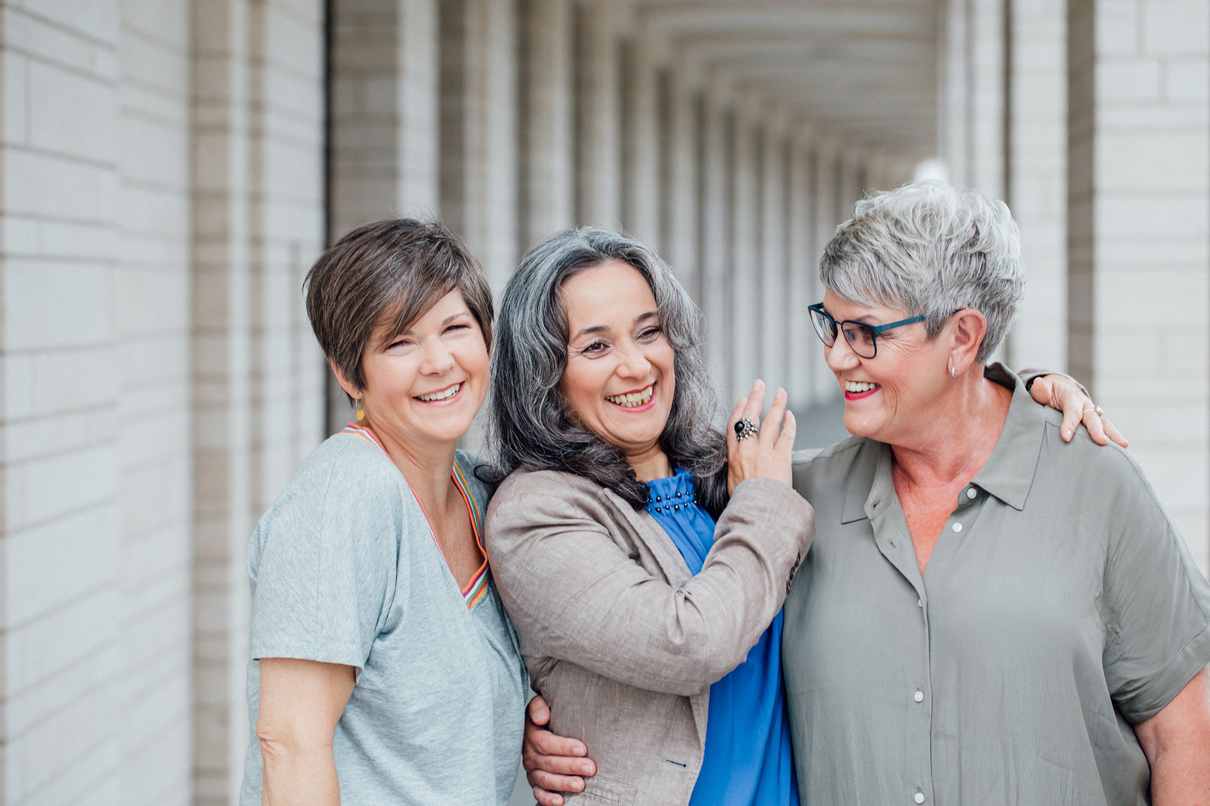 Drei Frauen mit kurzen und grauen Haaren stehen lachend Arm in Arm in einem hellen Säulengang, Fotoshooting für Colli Natur Friseure