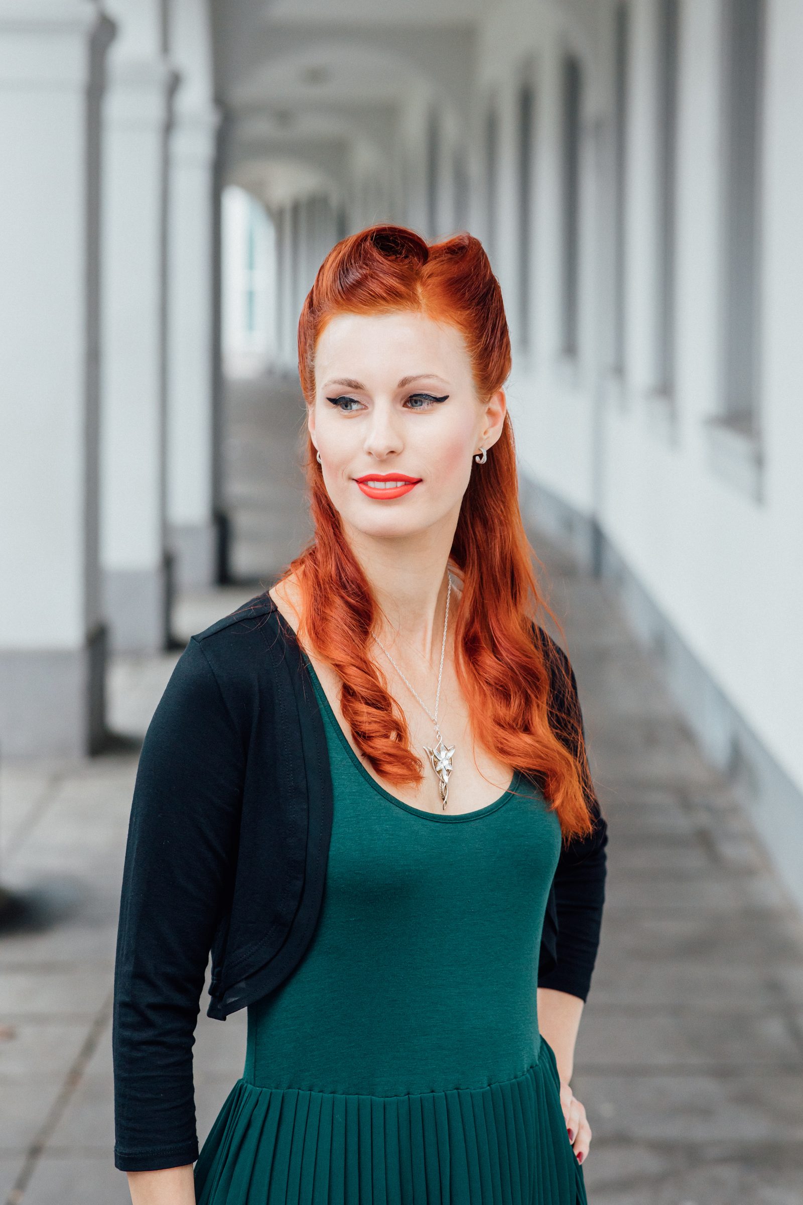 Frau mit langen roten Haaren in Wellen und grünem Kleid steht in einem hellen Säulengang, Fotoshooting für Colli Natur Friseure