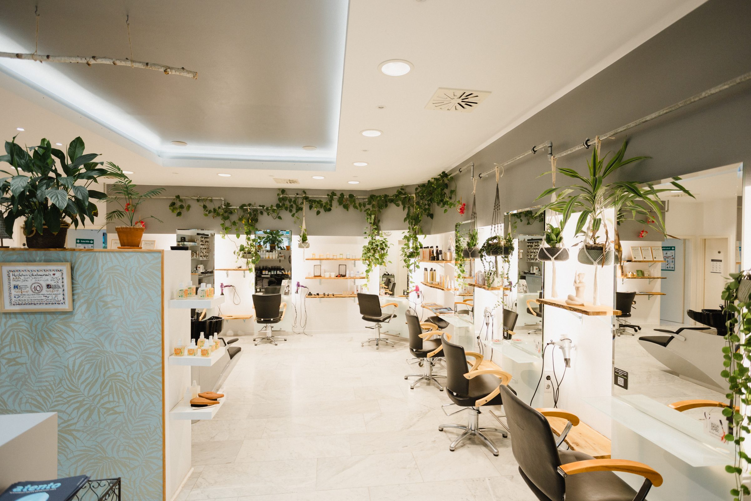 Heller, langgestreckter Friseursalon von Colli Natur Friseure mit Bedienplätzen, Holzablagen und vielen Grünpflanzen