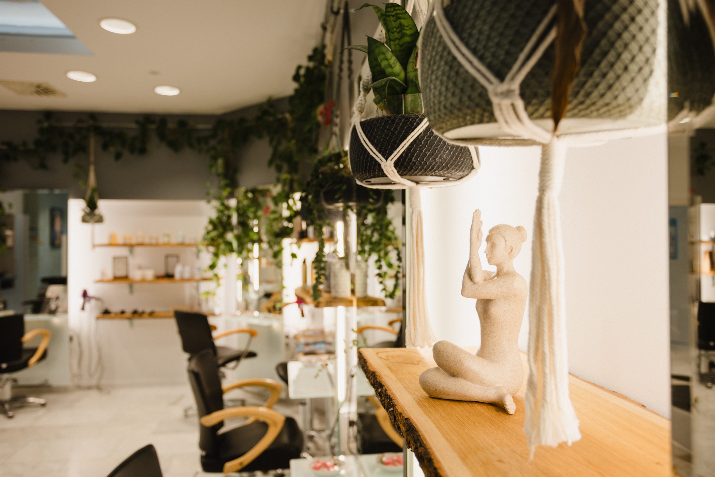 Detail im Salon von Colli Natur Friseure mit einer kleinen Figur auf einem Holzbrett, Makramee-Blumenampeln und Bedienplätzen im Hintergrund