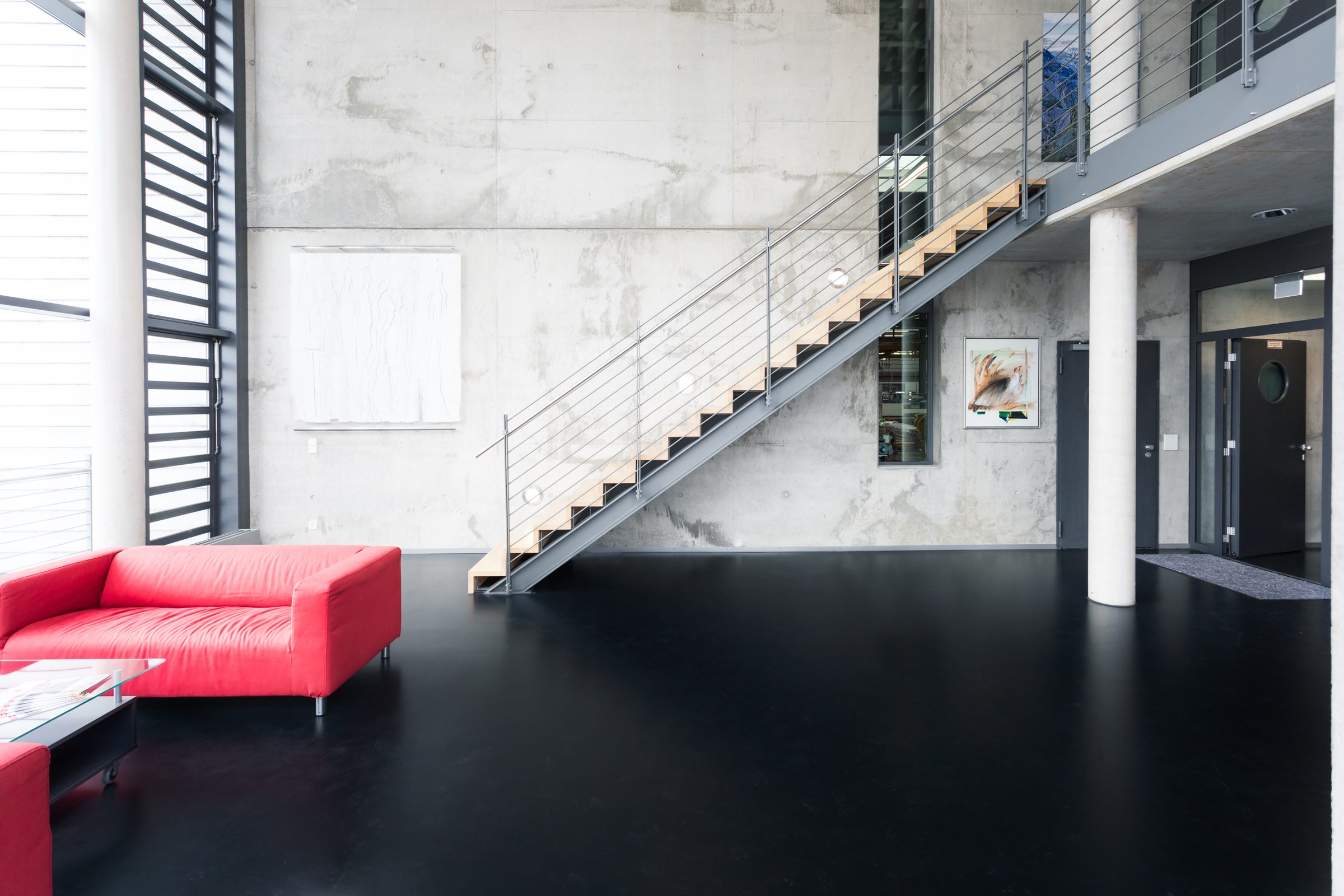 Foyer von Eugen Geyer mit Sichtbetonwand, Treppe mit Holzstufen und rotem Sofa