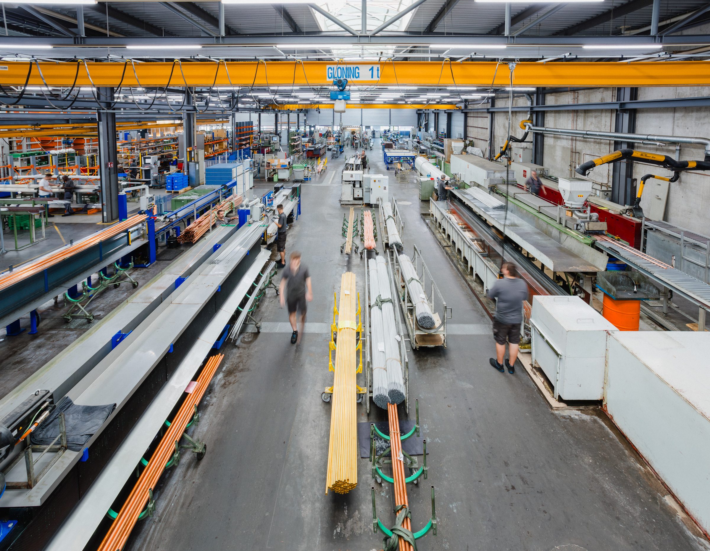 Blick von oben auf lange Fertigungslinien mit Kupfer- und Messingrohren in der Produktionshalle von Eugen Geyer, zwei Mitarbeiter gehen durch die Halle