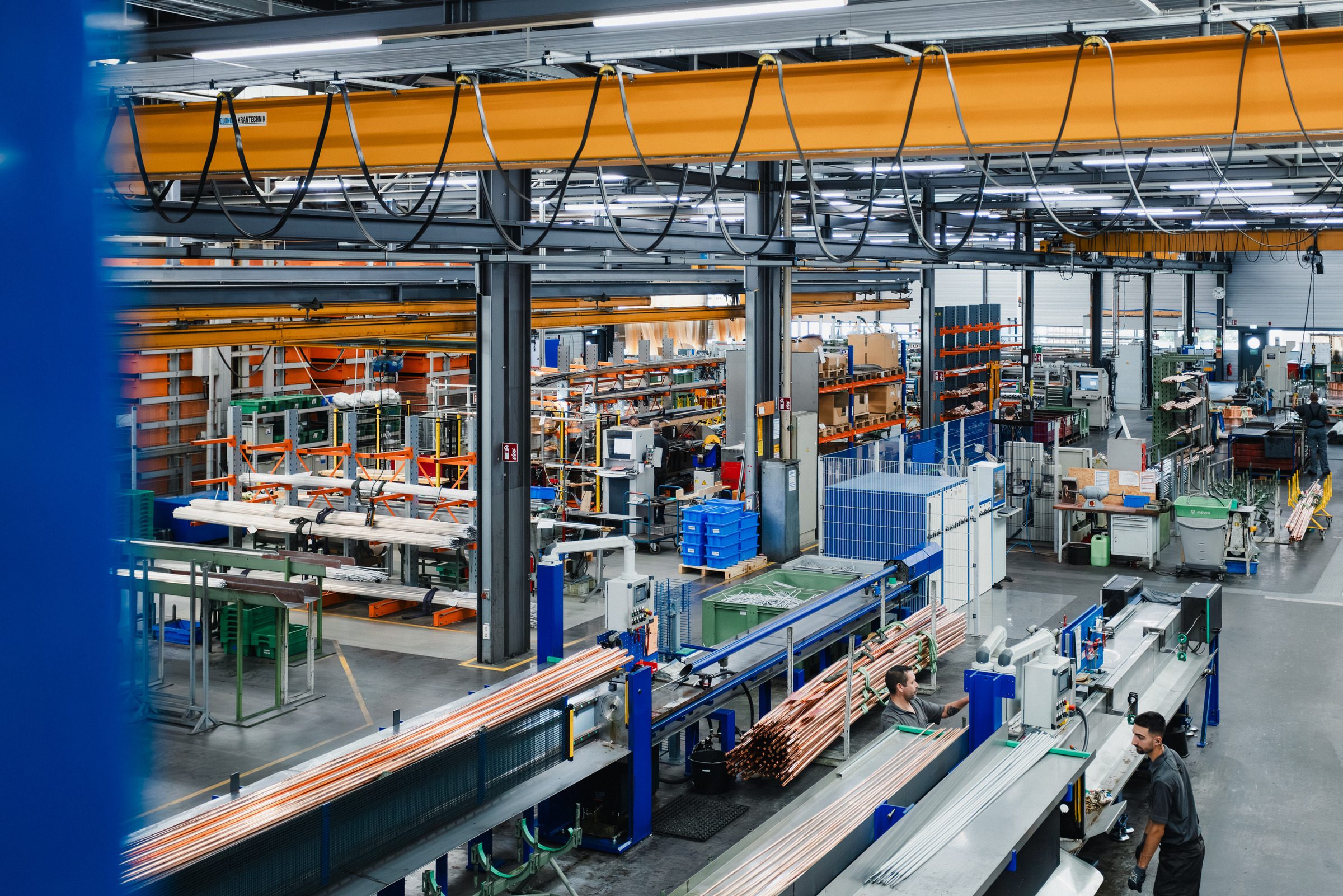 Produktionshalle von Eugen Geyer von einer Empore aus gesehen, vorn Kupferrohre auf einer Fertigungslinie, darüber ein orangefarbener Hallenkran
