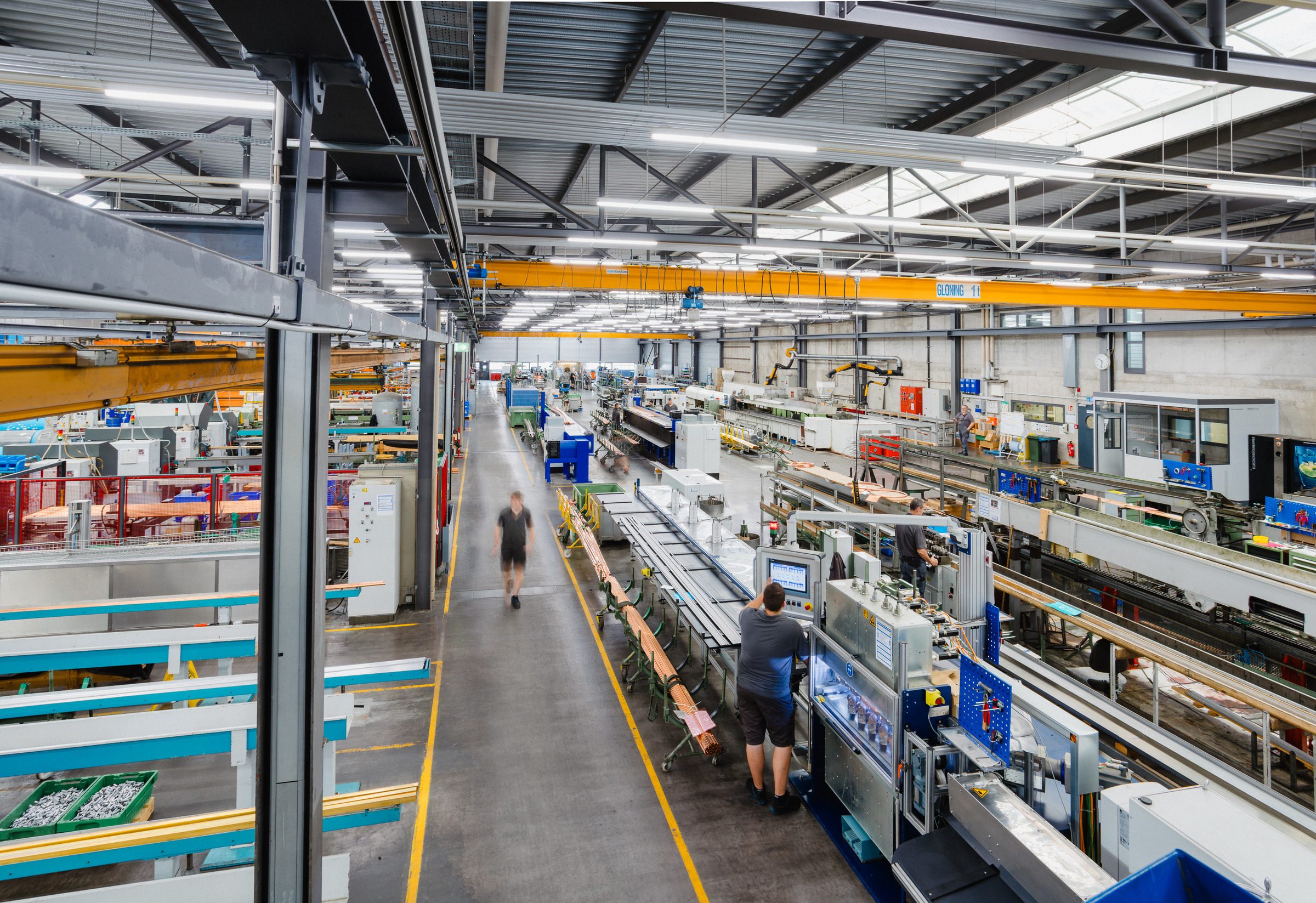 Langer Gang zwischen Fertigungslinien in der Produktionshalle von Eugen Geyer, rechts bedient ein Mitarbeiter eine Anlage