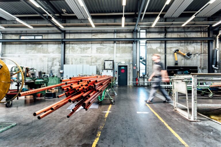 Produktionshalle von Eugen Geyer mit einem Bündel Kupferrohre im Vordergrund, dahinter geht ein Mitarbeiter vorbei