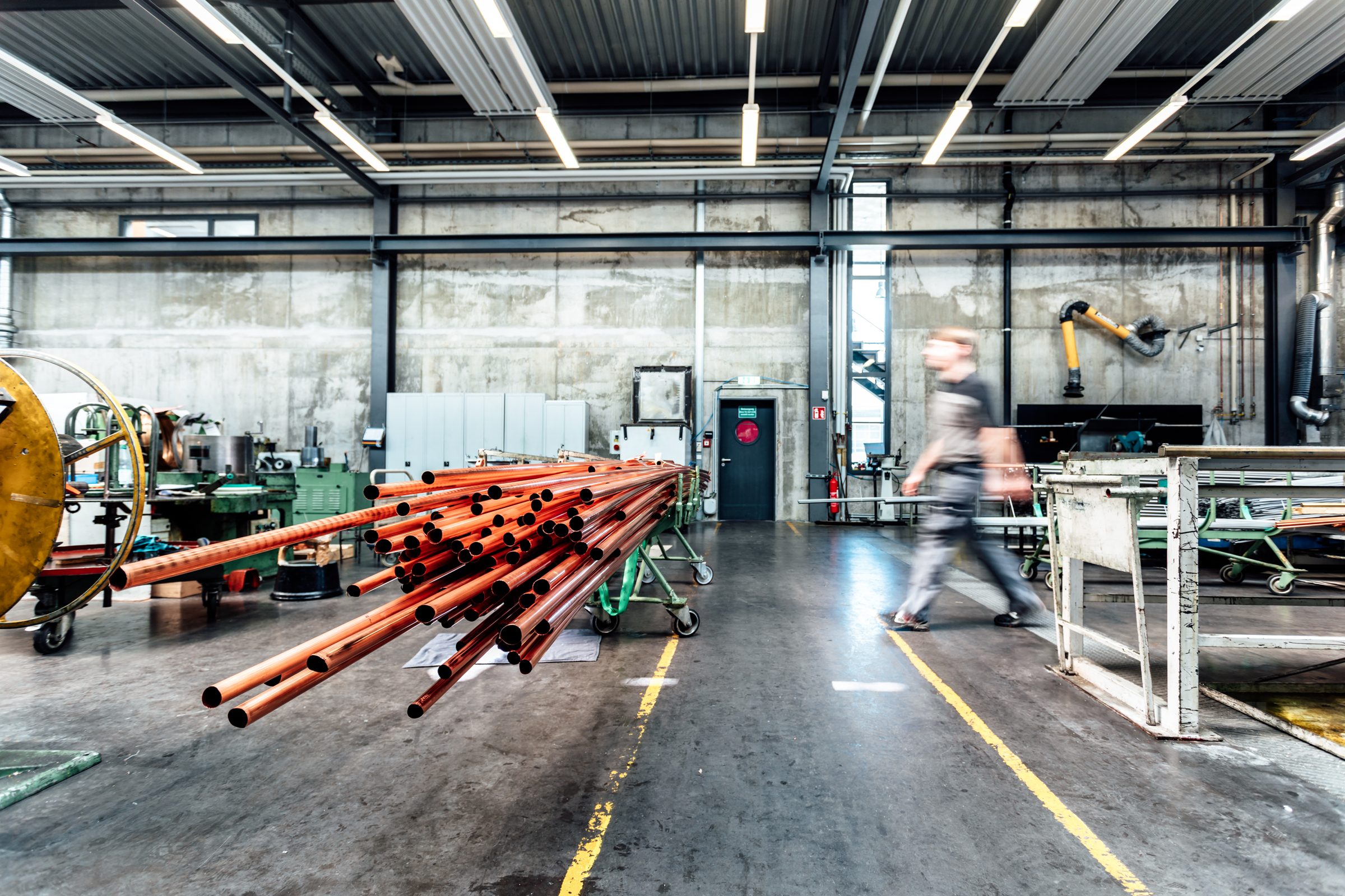 Produktionshalle von Eugen Geyer mit einem Bündel Kupferrohre im Vordergrund, dahinter geht ein Mitarbeiter vorbei