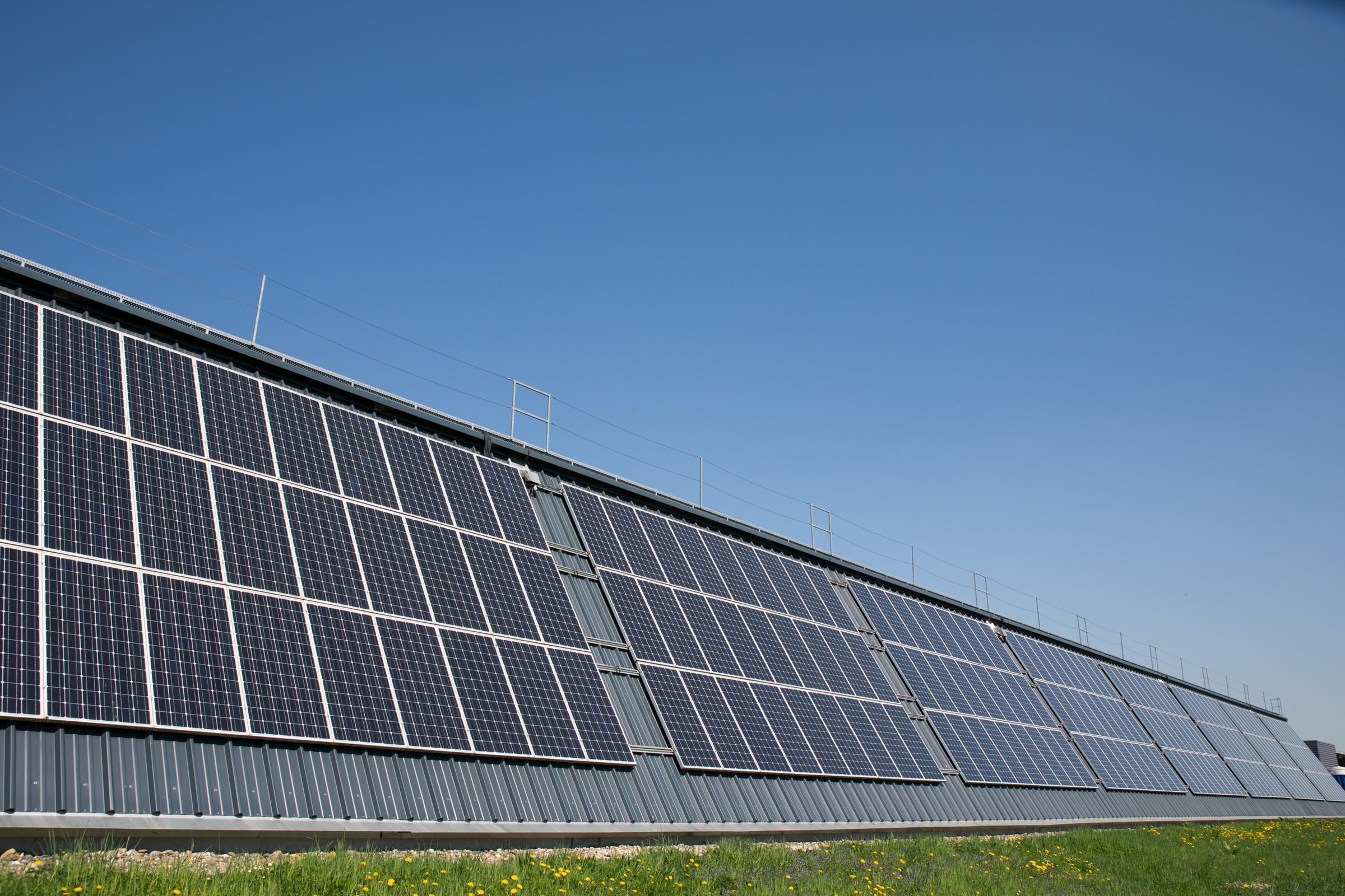 Lange Hallenfassade von Eugen Geyer mit Solarmodulen unter blauem Himmel
