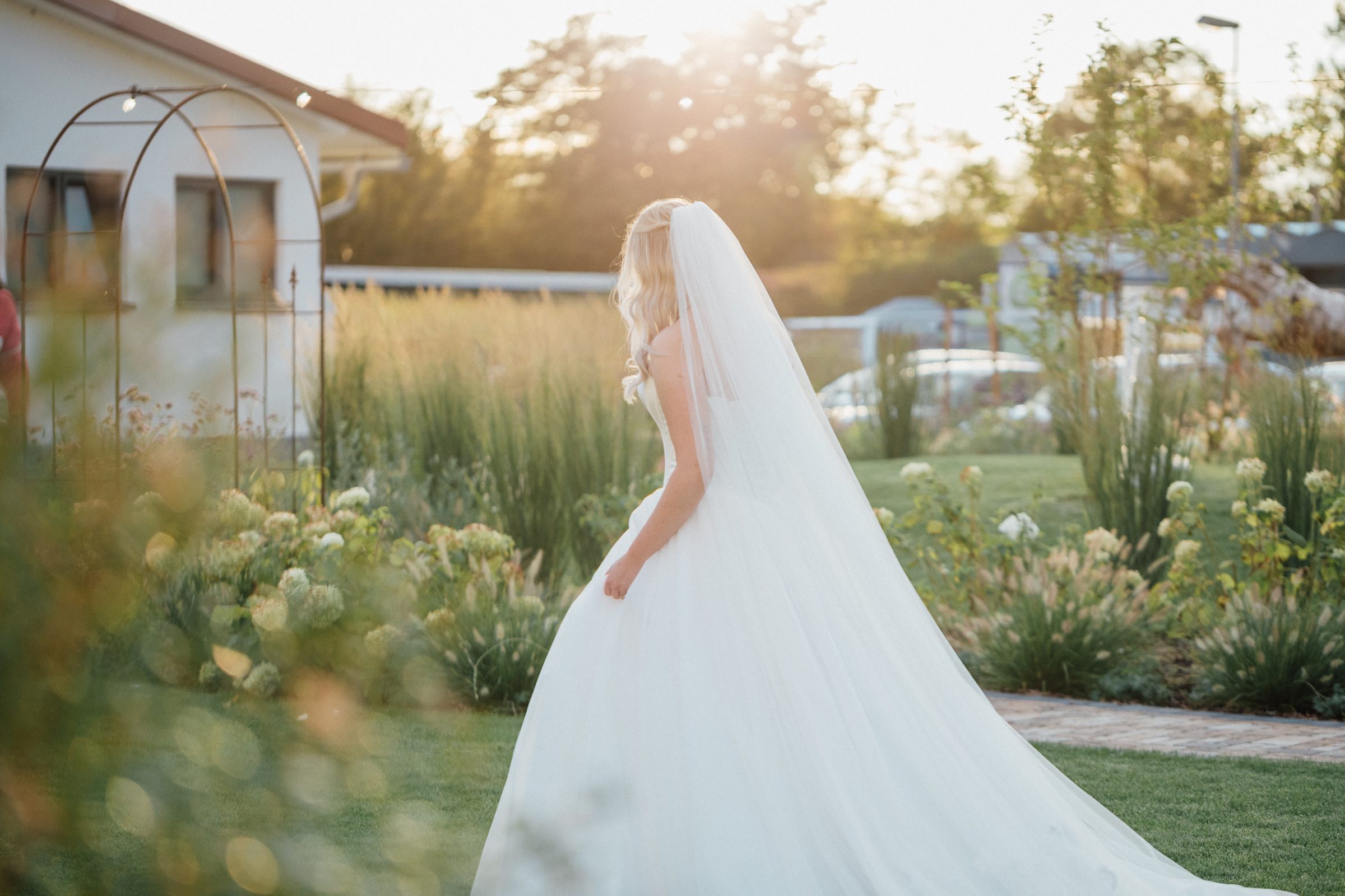 Braut mit langem Schleier von hinten im abendlichen Gegenlicht im Garten des Eventum beim Hotel Engelhorn