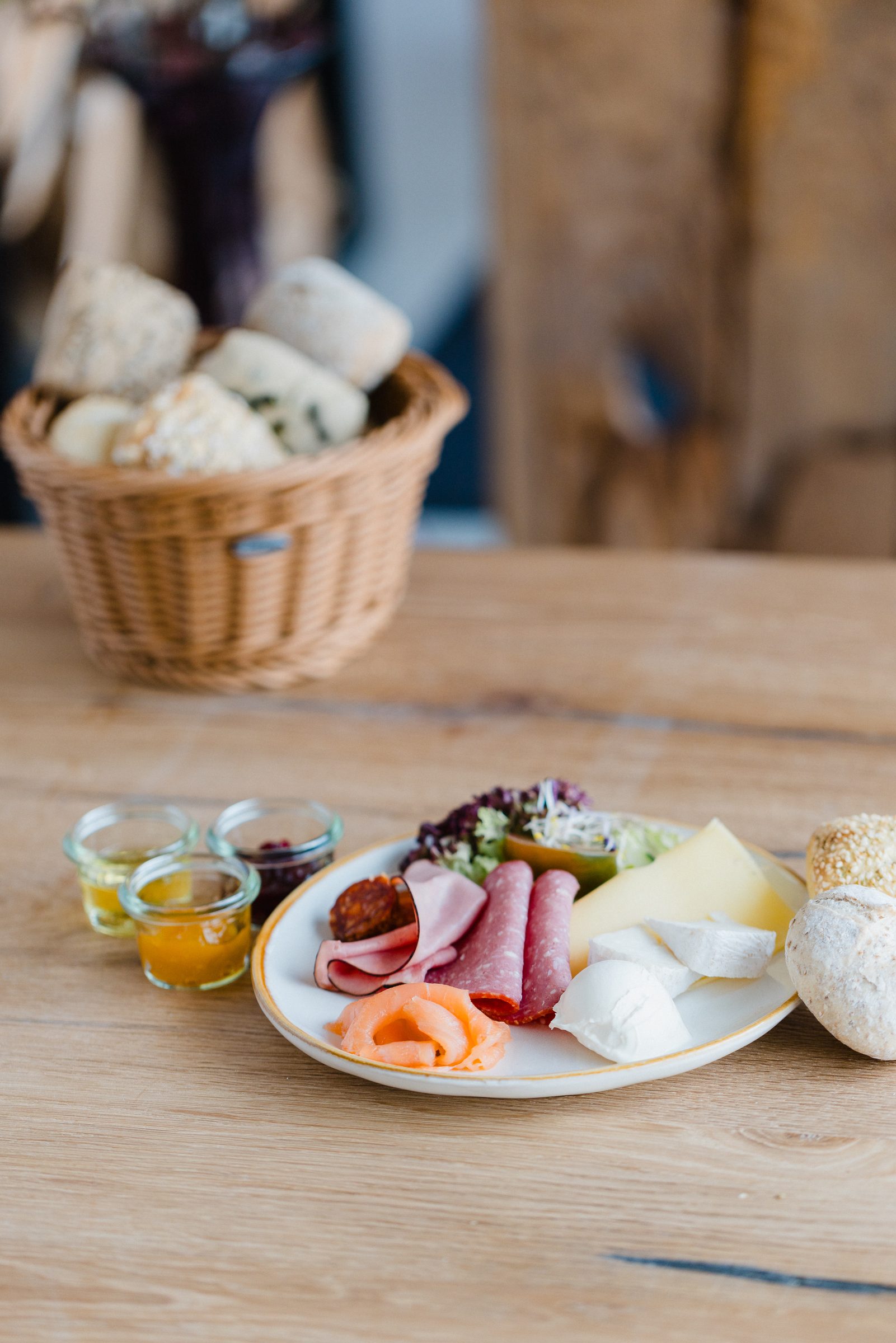 Frühstücksteller mit Schinken, Salami, Lachs und Käse, dazu Brotkorb, Honig und Marmelade auf einem Holztisch im Café Emilie des Hotel Engelhorn