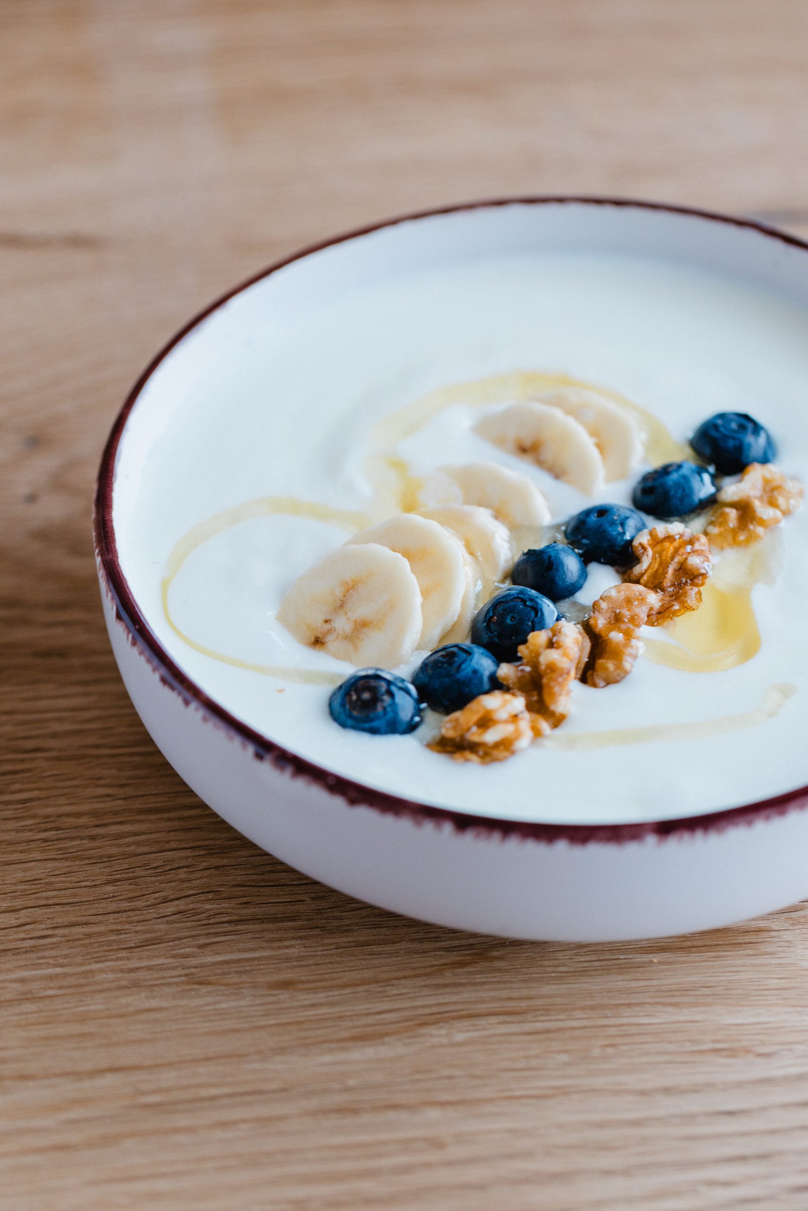 Schale mit Joghurt, Bananenscheiben, Heidelbeeren, Walnüssen und Honig auf einem Holztisch im Café Emilie des Hotel Engelhorn