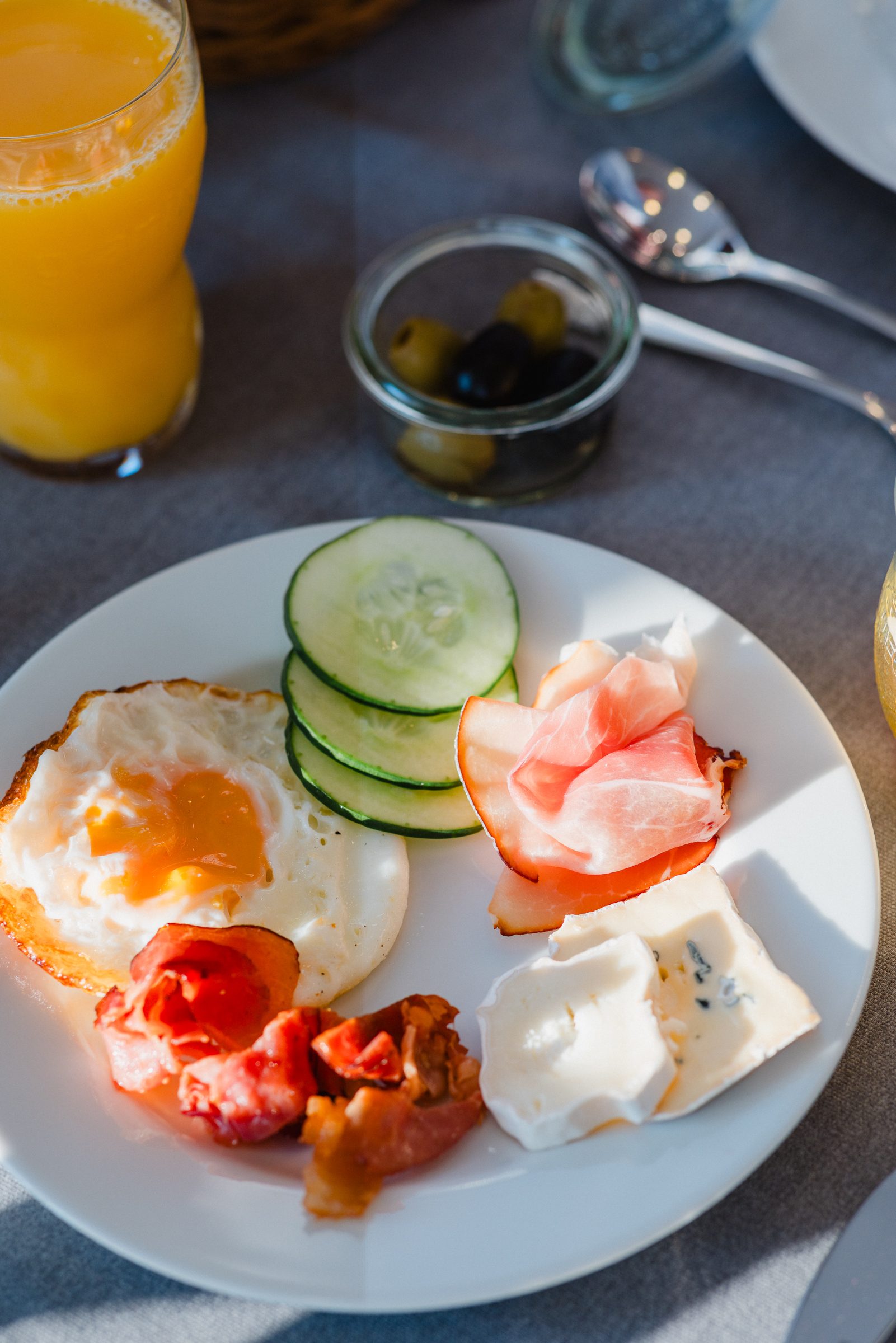 Frühstücksteller mit Spiegelei, Gurke, Schinken und Käse im Hotel Engelhorn, daneben Orangensaft und Oliven