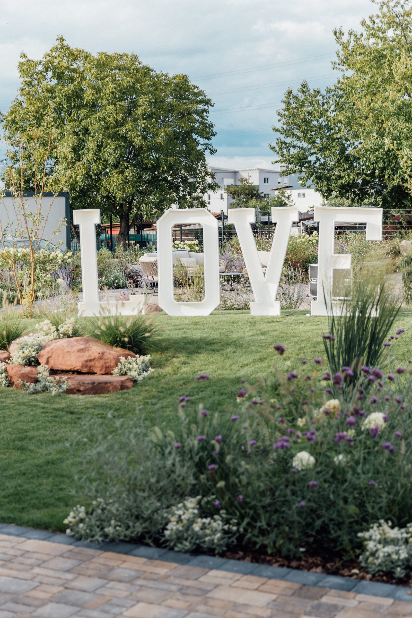 Große weiße Buchstaben LOVE auf dem Rasen im Garten des Eventum beim Hotel Engelhorn, davor Blumenbeete und Steine