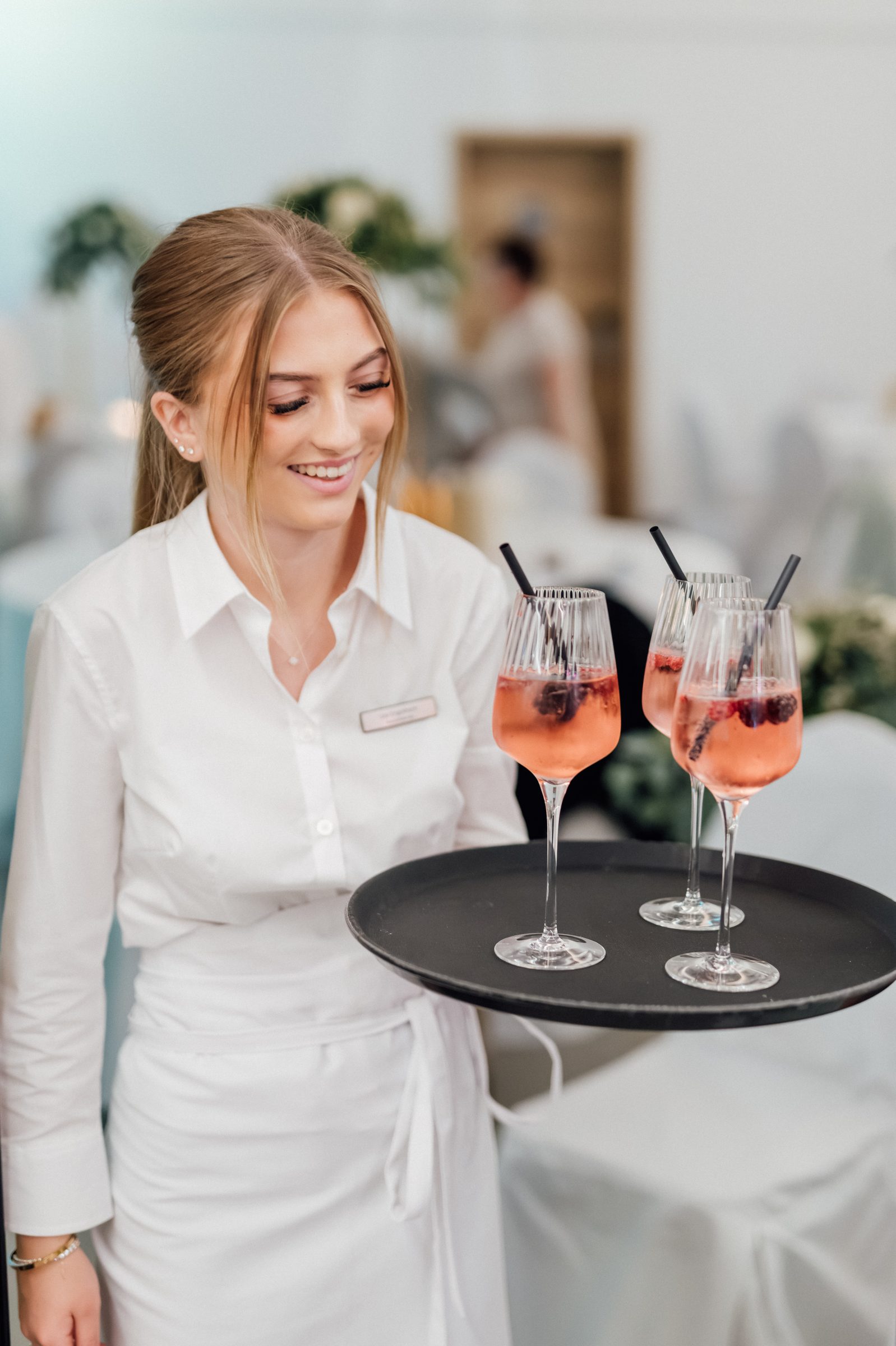 Servicemitarbeiterin des Hotel Engelhorn trägt bei einer Hochzeitsfeier ein Tablett mit rosafarbenen Aperitifs