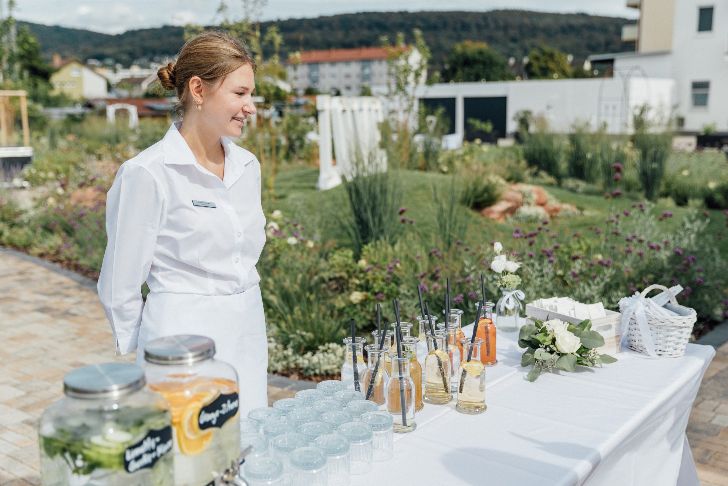 Servicemitarbeiterin des Hotel Engelhorn an einem Getränketisch mit Gläsern, Flaschen und Getränkespendern im Garten bei einer Hochzeit