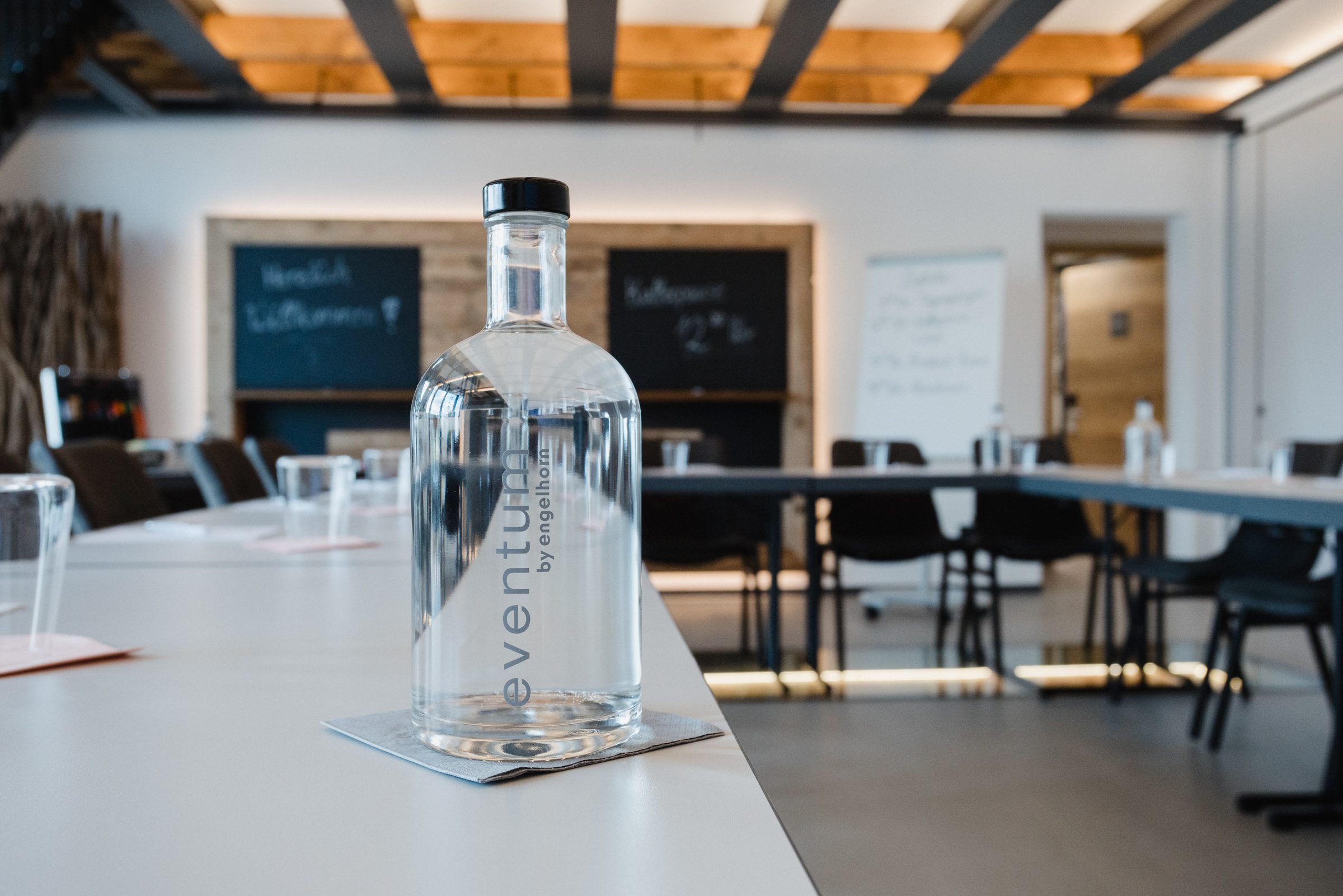 Wasserflasche mit Eventum-Aufdruck auf einem Tagungstisch im Hotel Engelhorn, dahinter Tische in U-Form und Tafeln