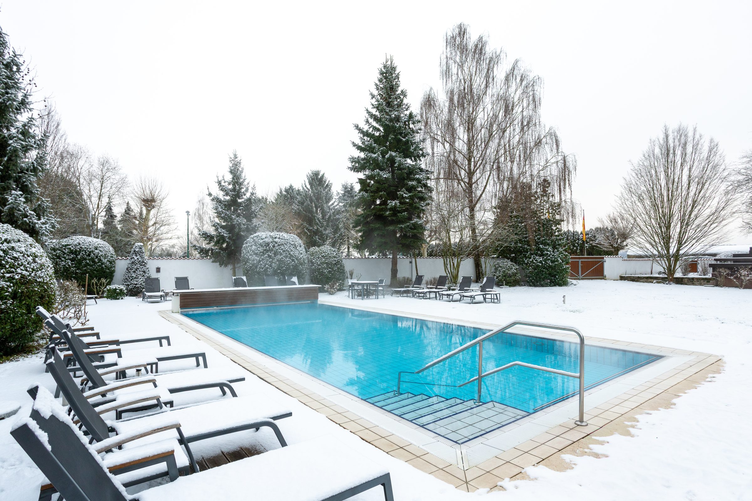 Außenpool des Hotel Krone im Winter, Liegen, Büsche und Bäume im Garten sind verschneit