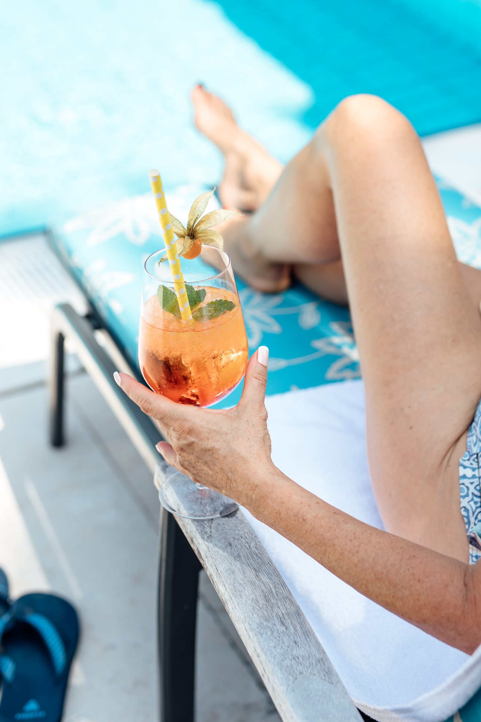 Hand hält einen Spritz mit Minze, Physalis und Strohhalm auf einer Liege am Außenpool des Hotel Krone