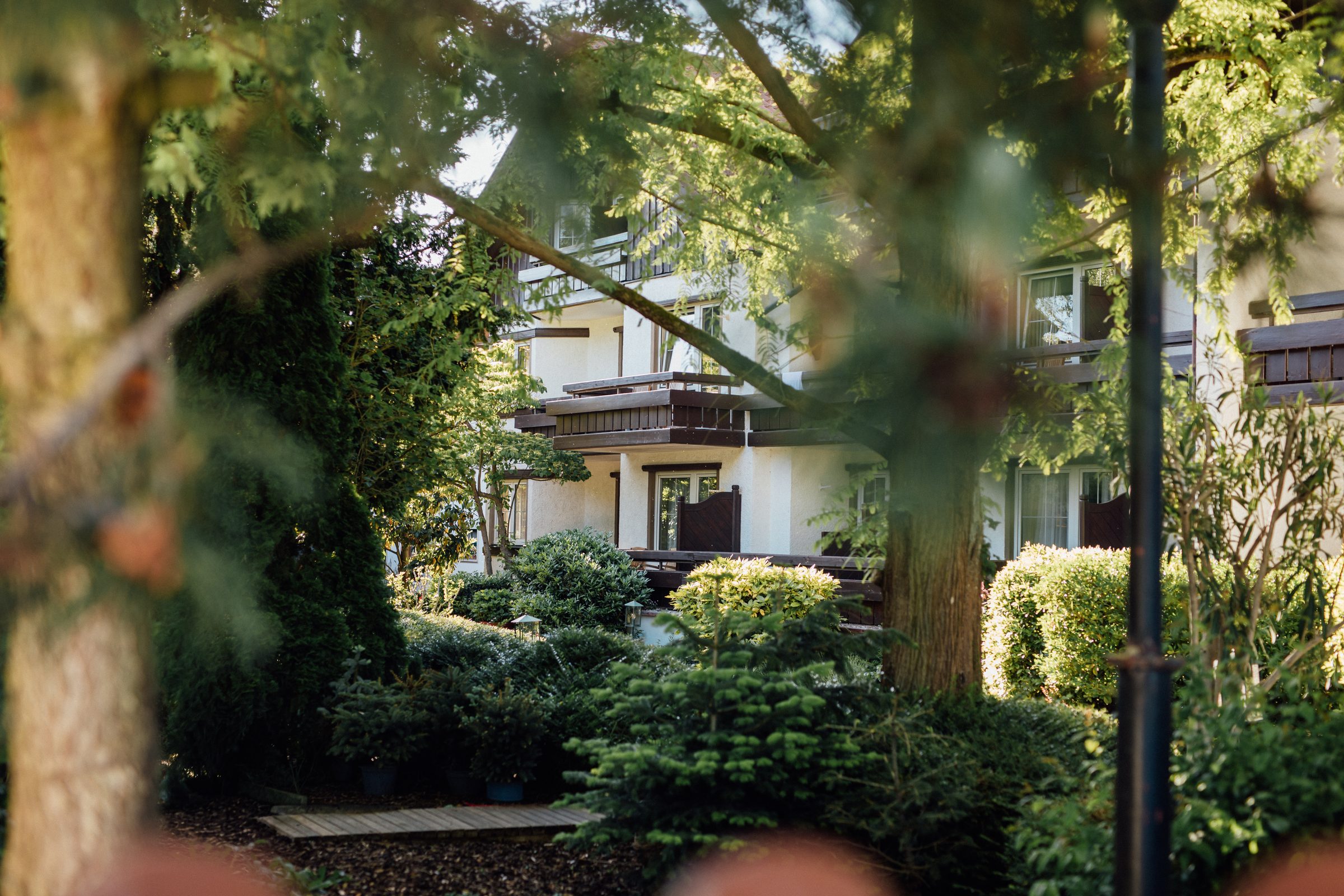 Garten des Hotel Krone mit Bäumen und Hecken, dahinter das Haus mit Holzbalkonen