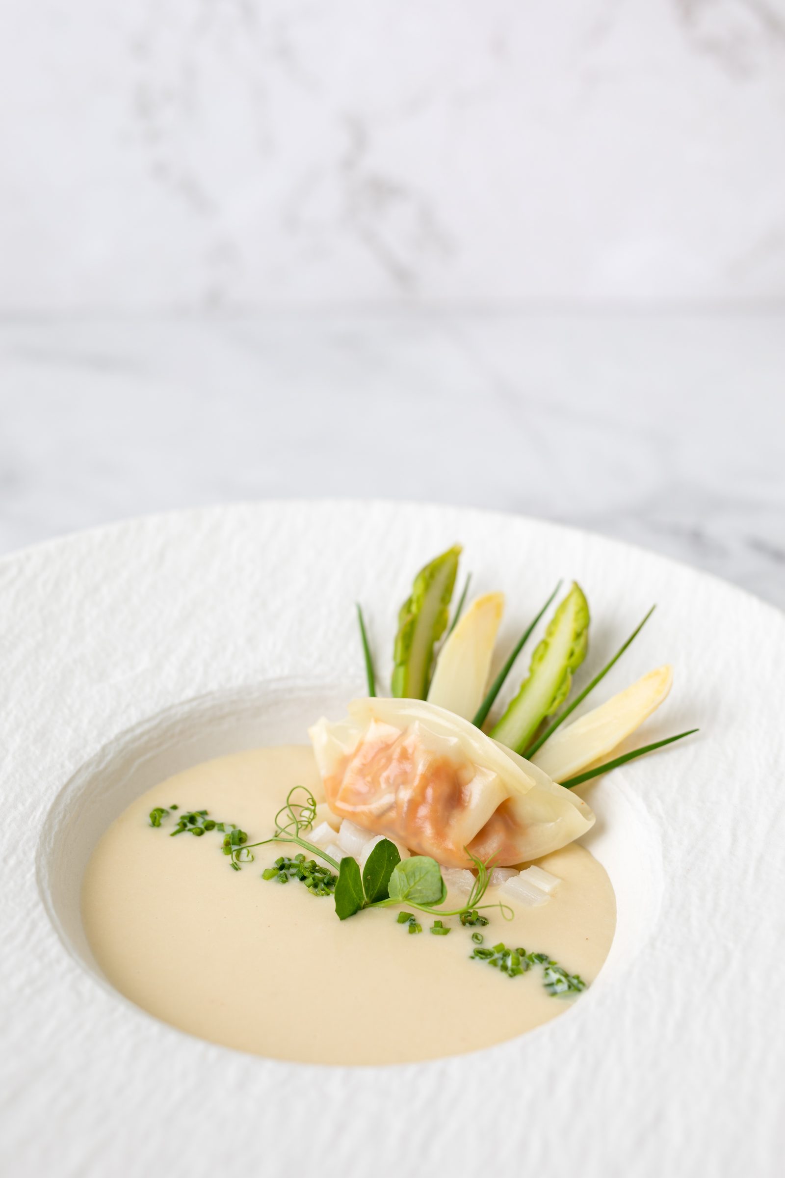 Teigtasche mit weißem und grünem Spargel auf heller Sauce in einem weißen Teller