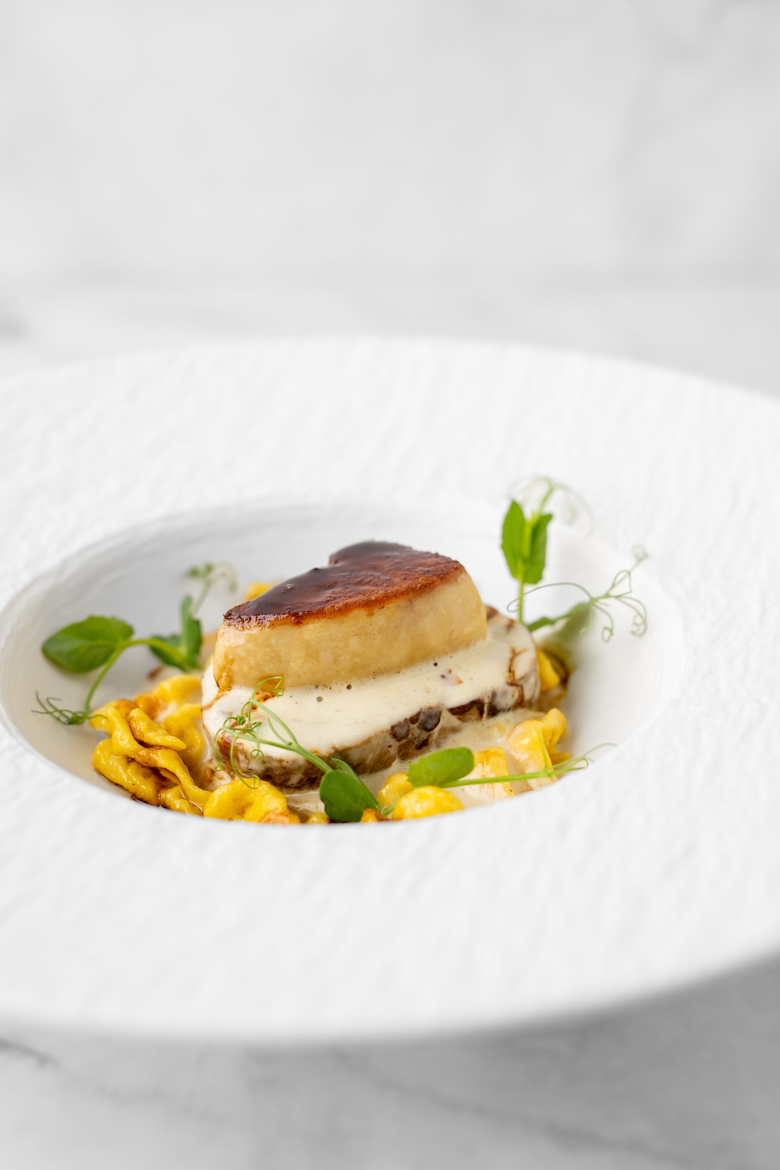 Glasierte Tranche auf Bandnudeln mit heller Sauce und Erbsenranken in einem tiefen weißen Teller
