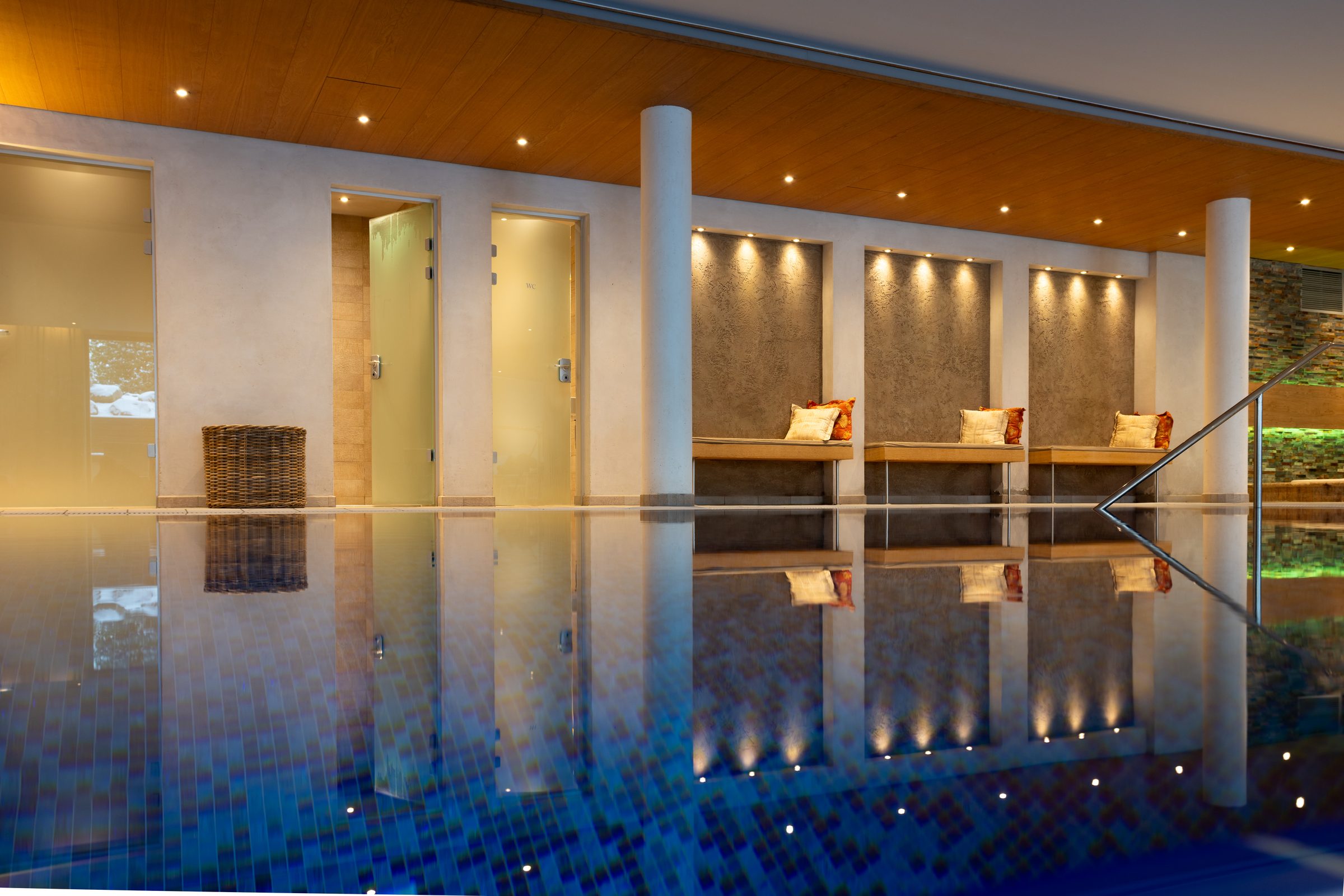 Beleuchteter Innenpool im Hotel Krone, die Ruheliegen in den Wandnischen spiegeln sich im Wasser