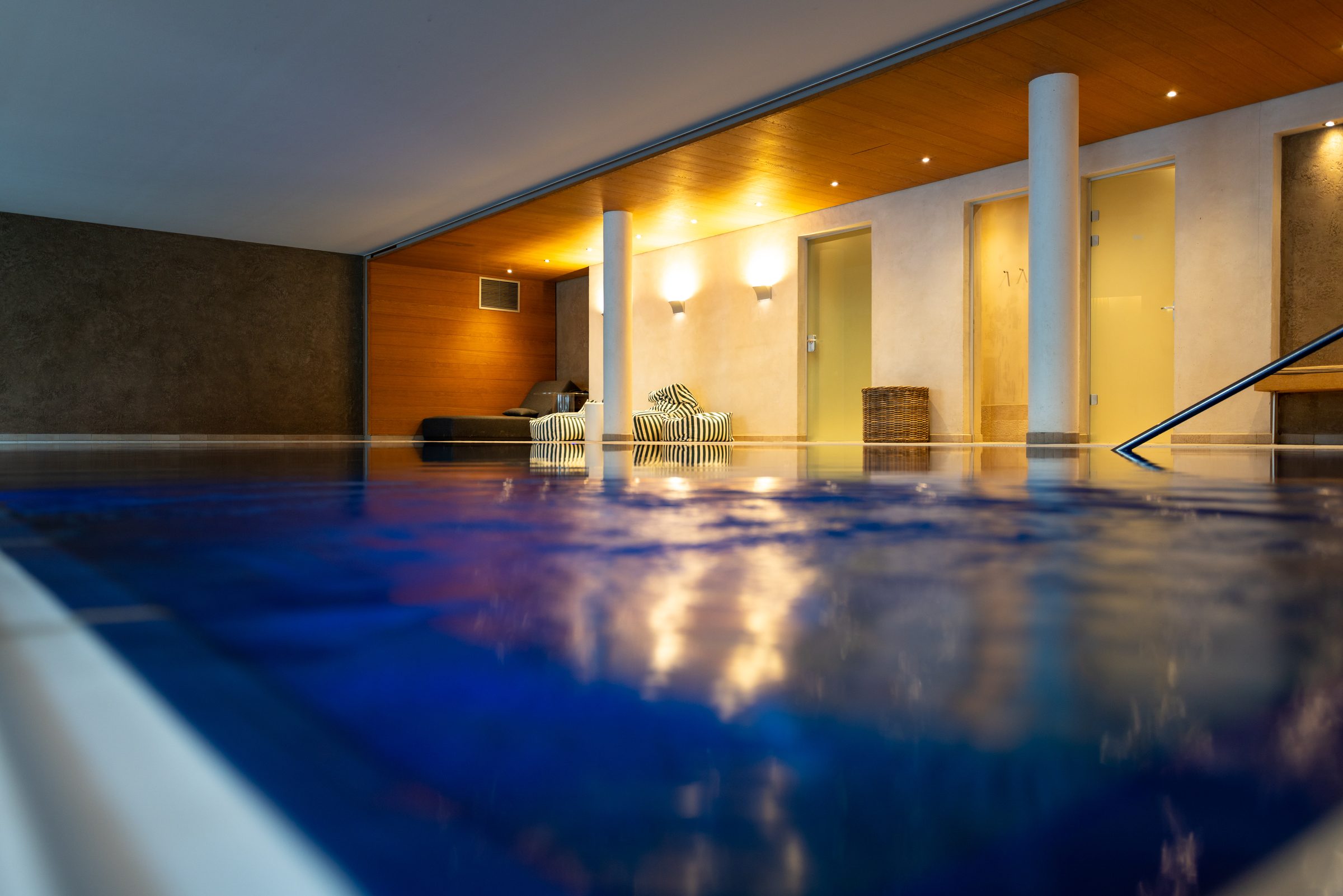 Blauer Innenpool im Hotel Krone knapp über der Wasserfläche fotografiert, dahinter Säulen, Liegen und warm beleuchtete Wände