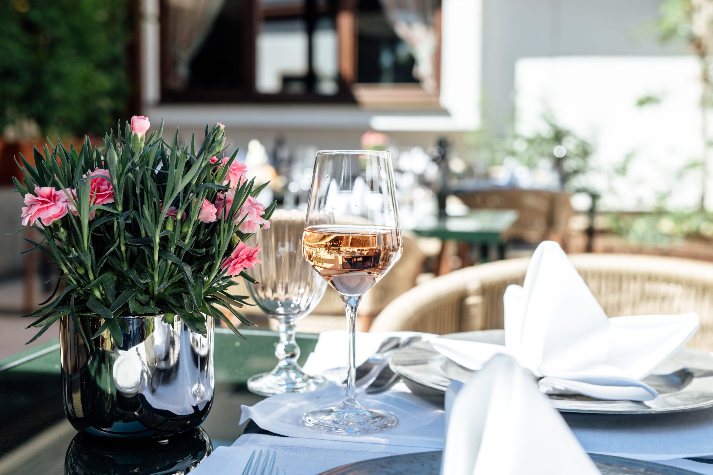 Gedeckter Tisch im Restaurant des Hotel Krone mit einem Glas Roséwein, gefalteten Servietten und rosa Nelken in einer silbernen Vase