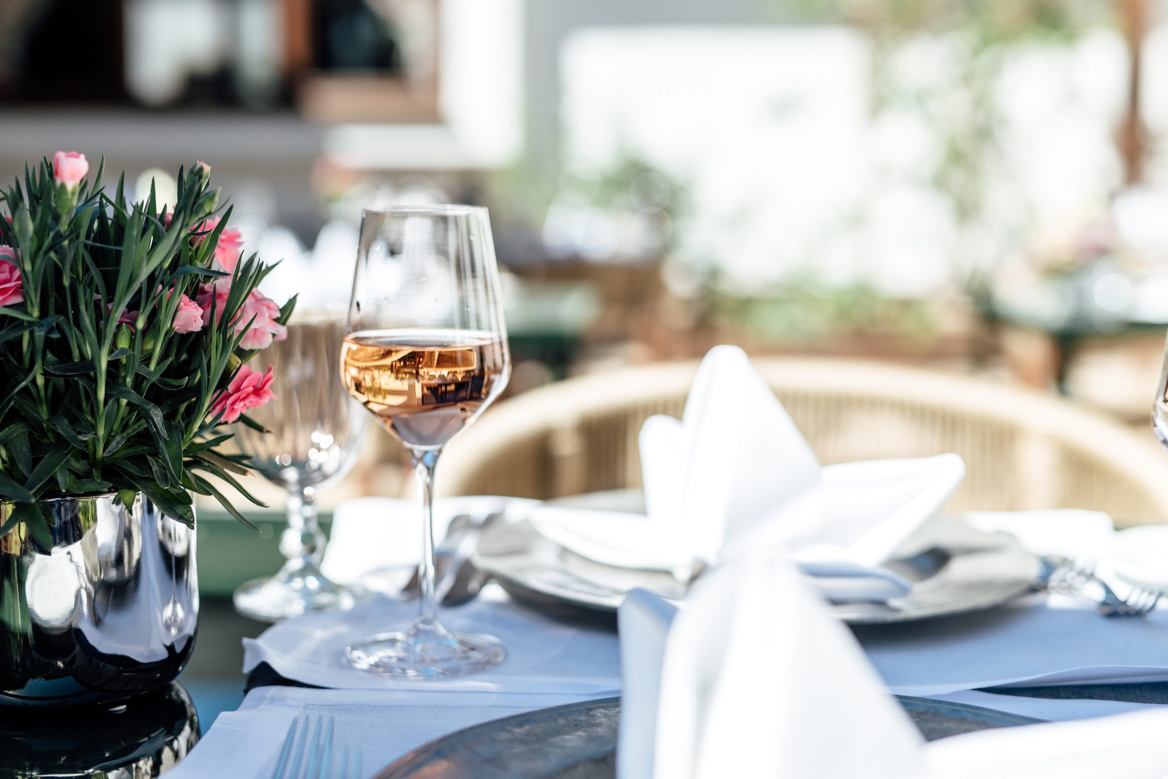 Gedeckter Tisch im Restaurant des Hotel Krone mit einem Glas Roséwein, weißen Servietten und rosa Nelken im Gegenlicht